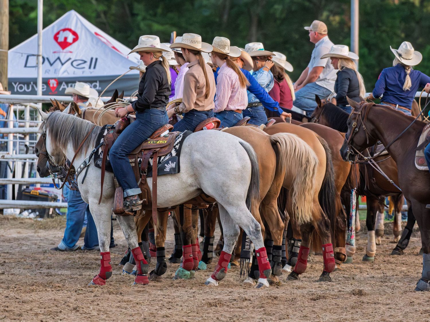 Group of rodeo riders on horses lined up wearing cowboy hats at outdoor equestrian event.