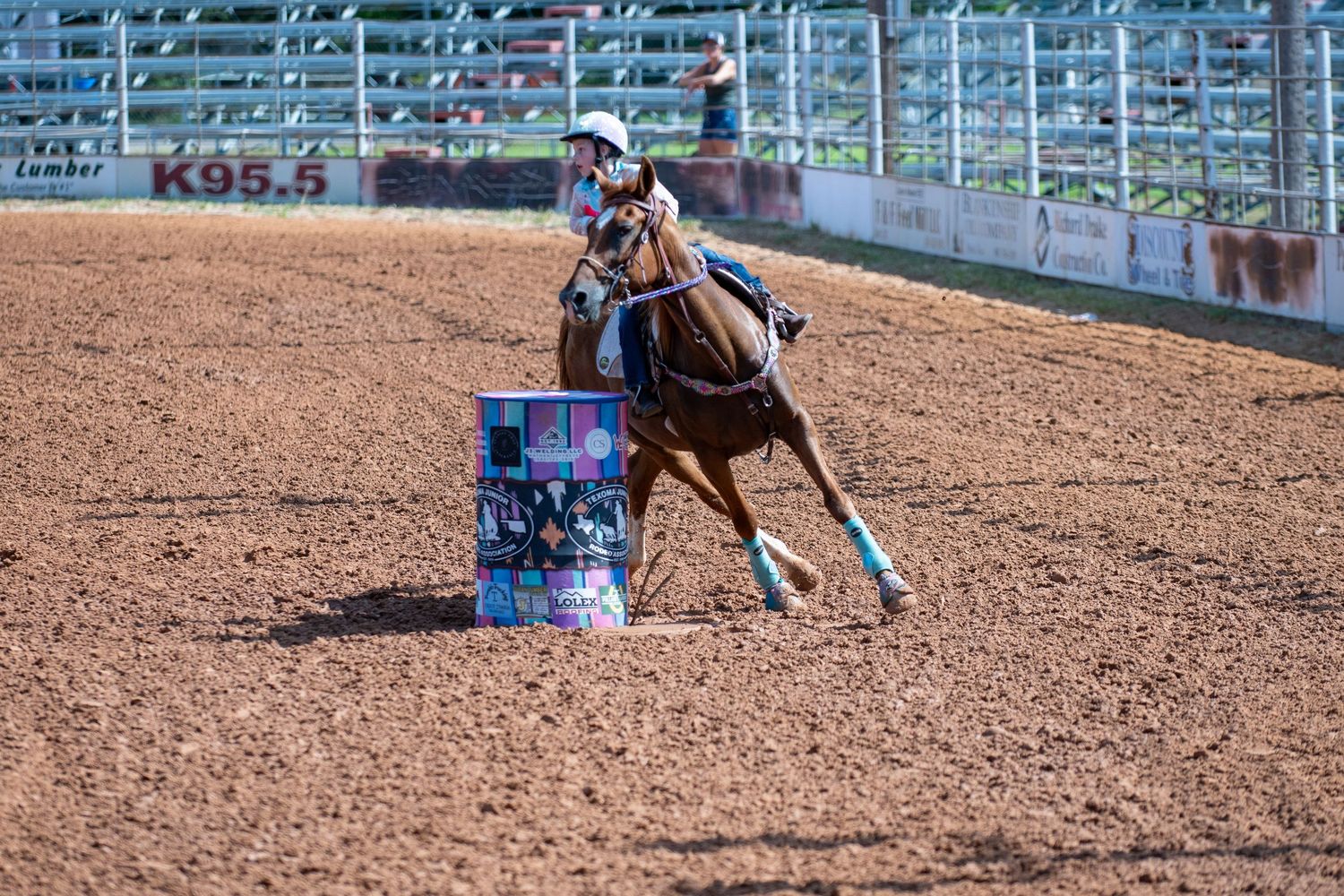 Barrel racing competitor on horseback navigating around a colorful decorated barrel in a rodeo.