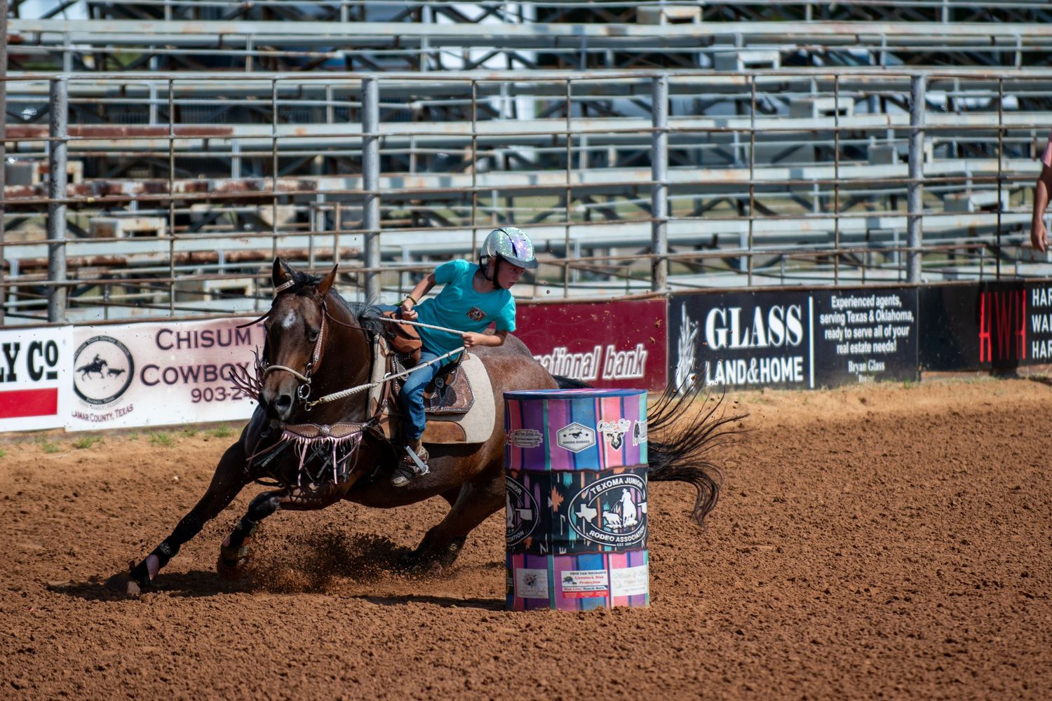 Barrel racer on horseback making a sharp turn around a decorated barrel in a rodeo arena.