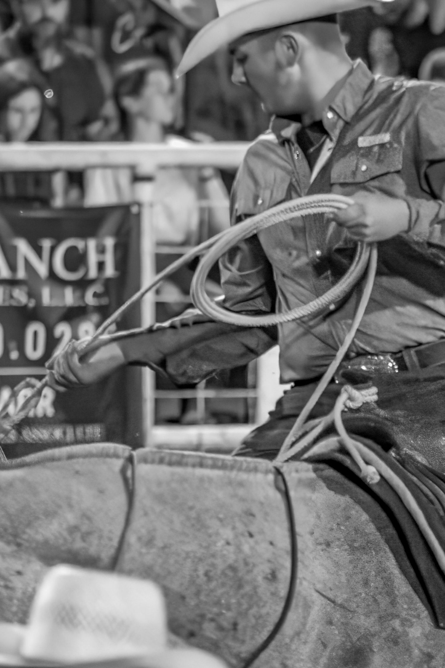 Black and white photo of a cowboy holding a lasso rope while seated on horseback at a rodeo event.
