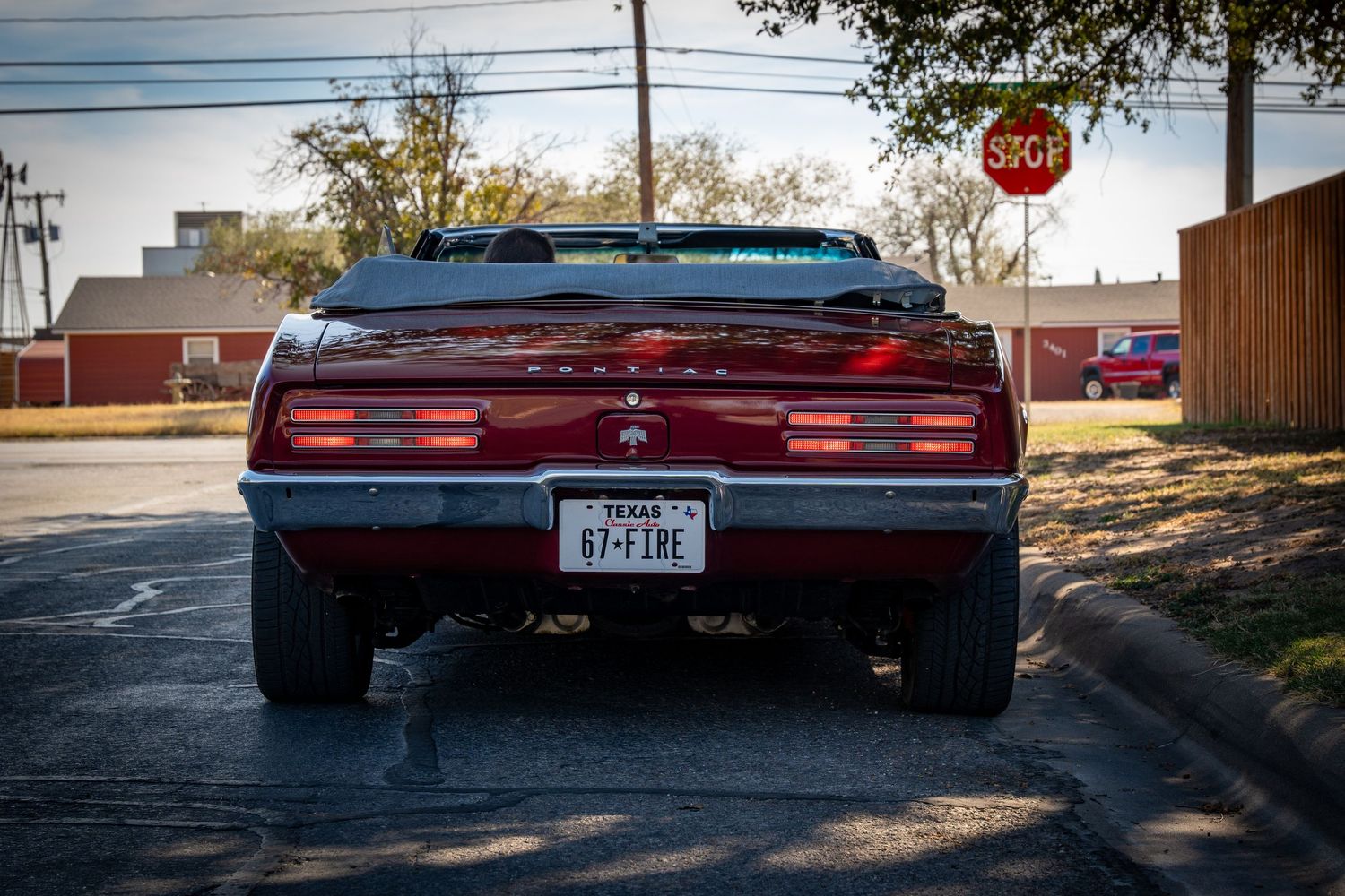 Rear view of a red Pontiac Firebird convertible with Texas license plate 67-FIRE at a street corner.