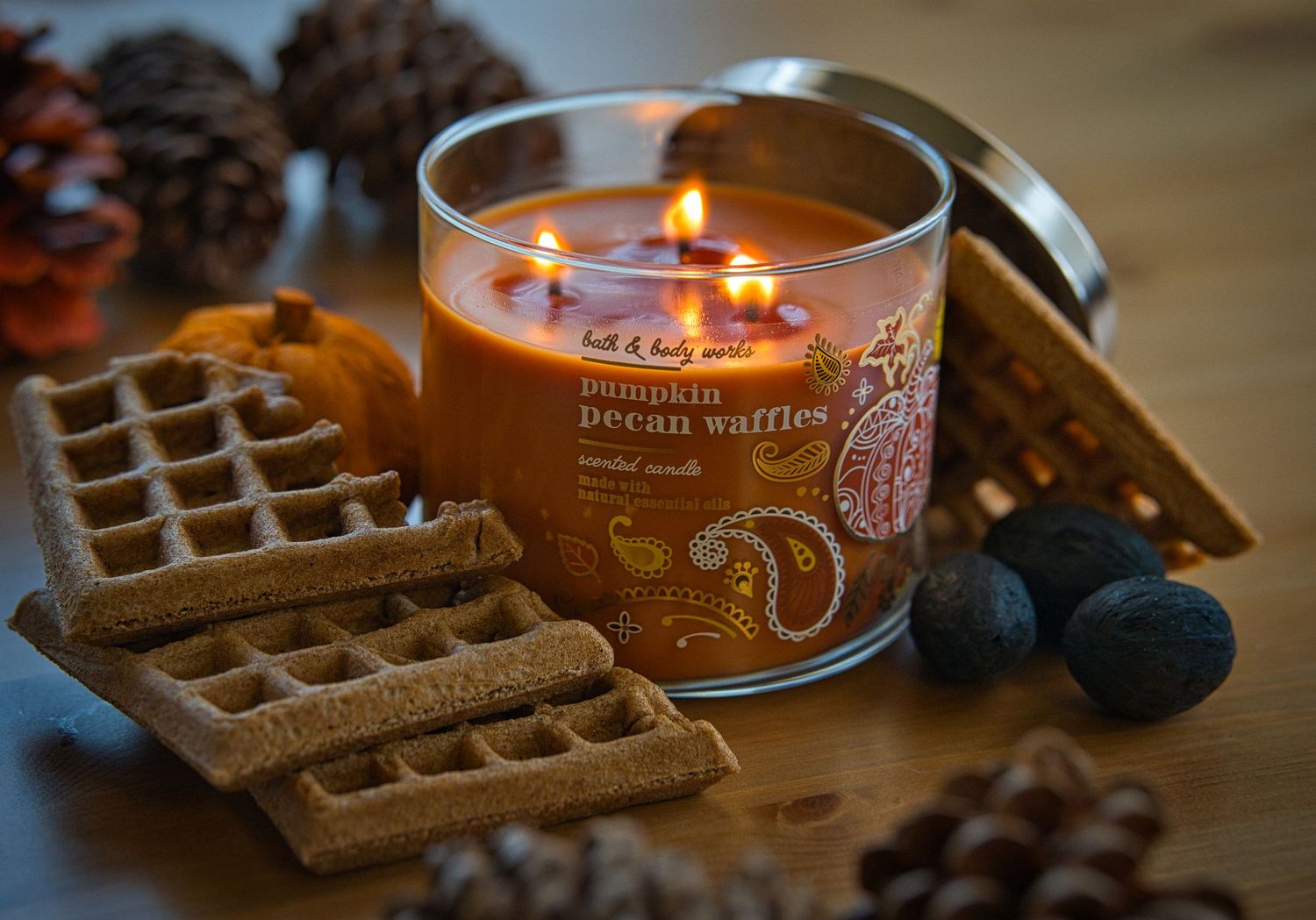 Bath & Body Works pumpkin pecan waffles candle lit surrounded by waffles, pinecones, and nuts.