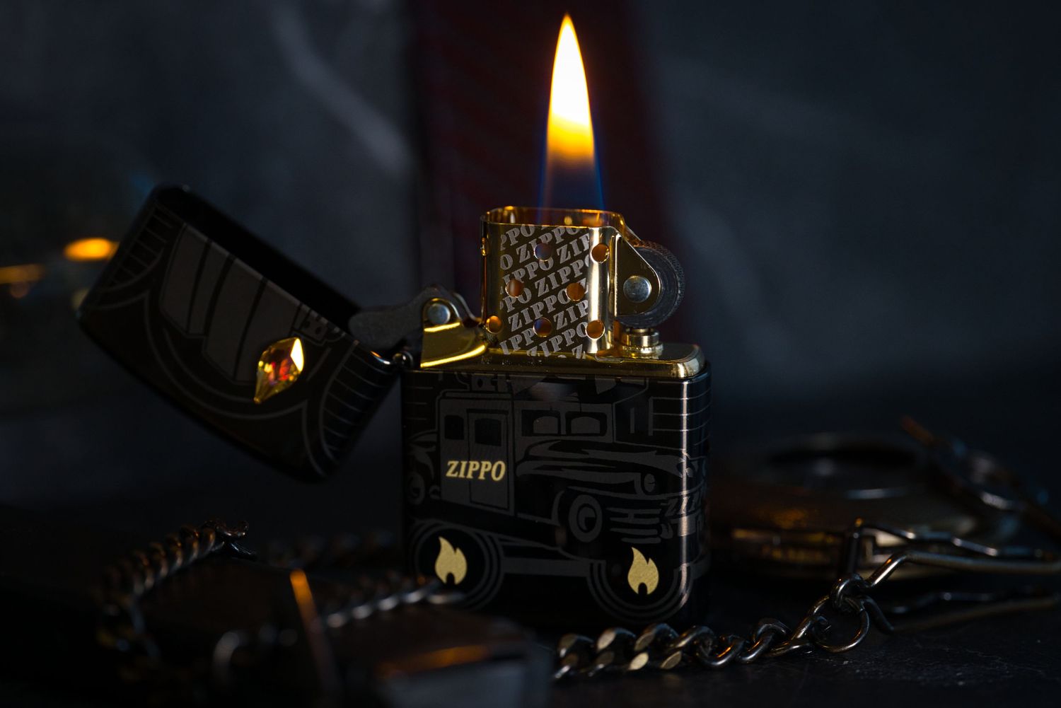 Lit Zippo lighter with engraved design glowing in dark with chain and reflective surface.