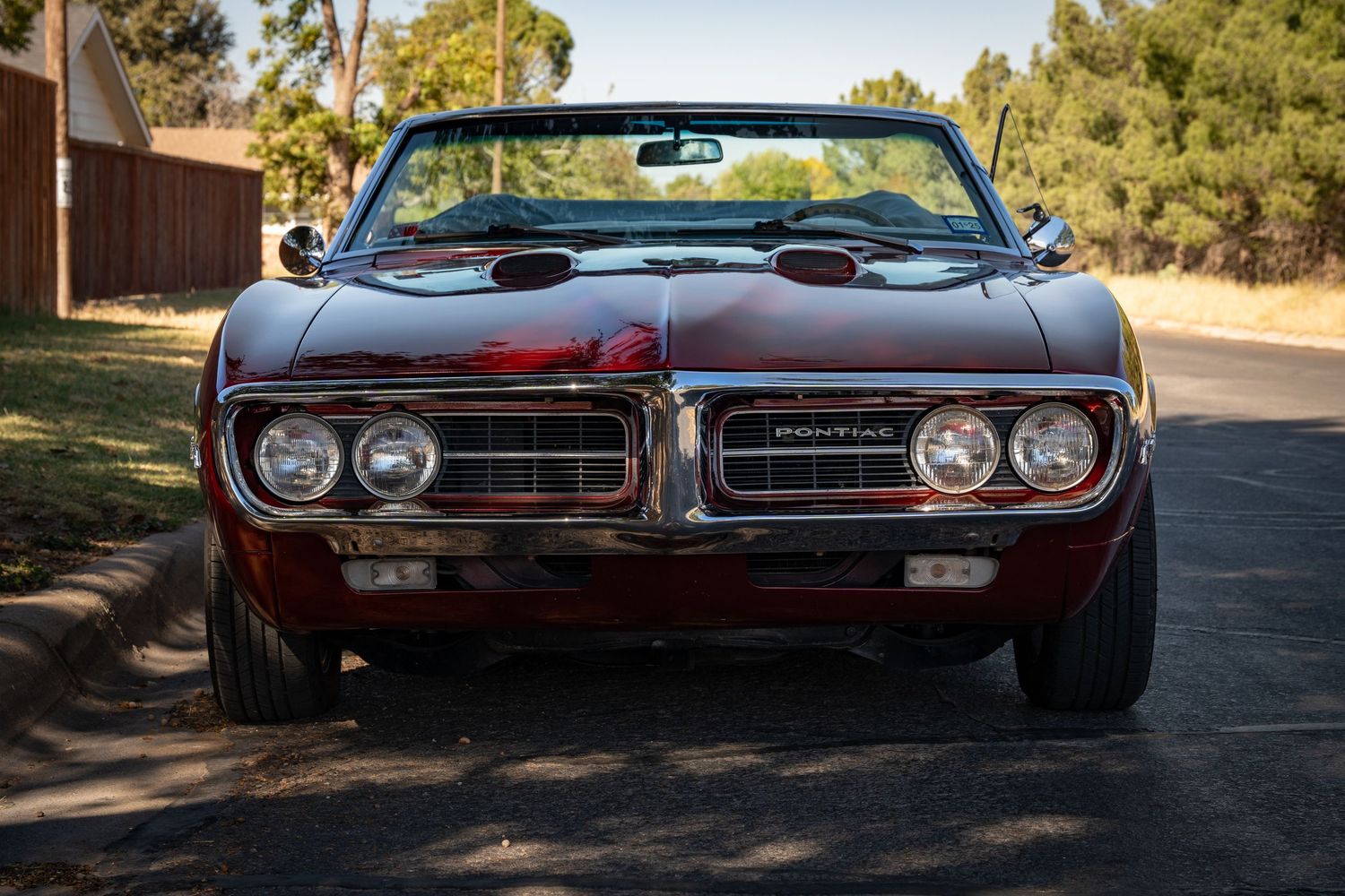 Front view of a restored red Pontiac Firebird convertible parked on a sunny driveway.
