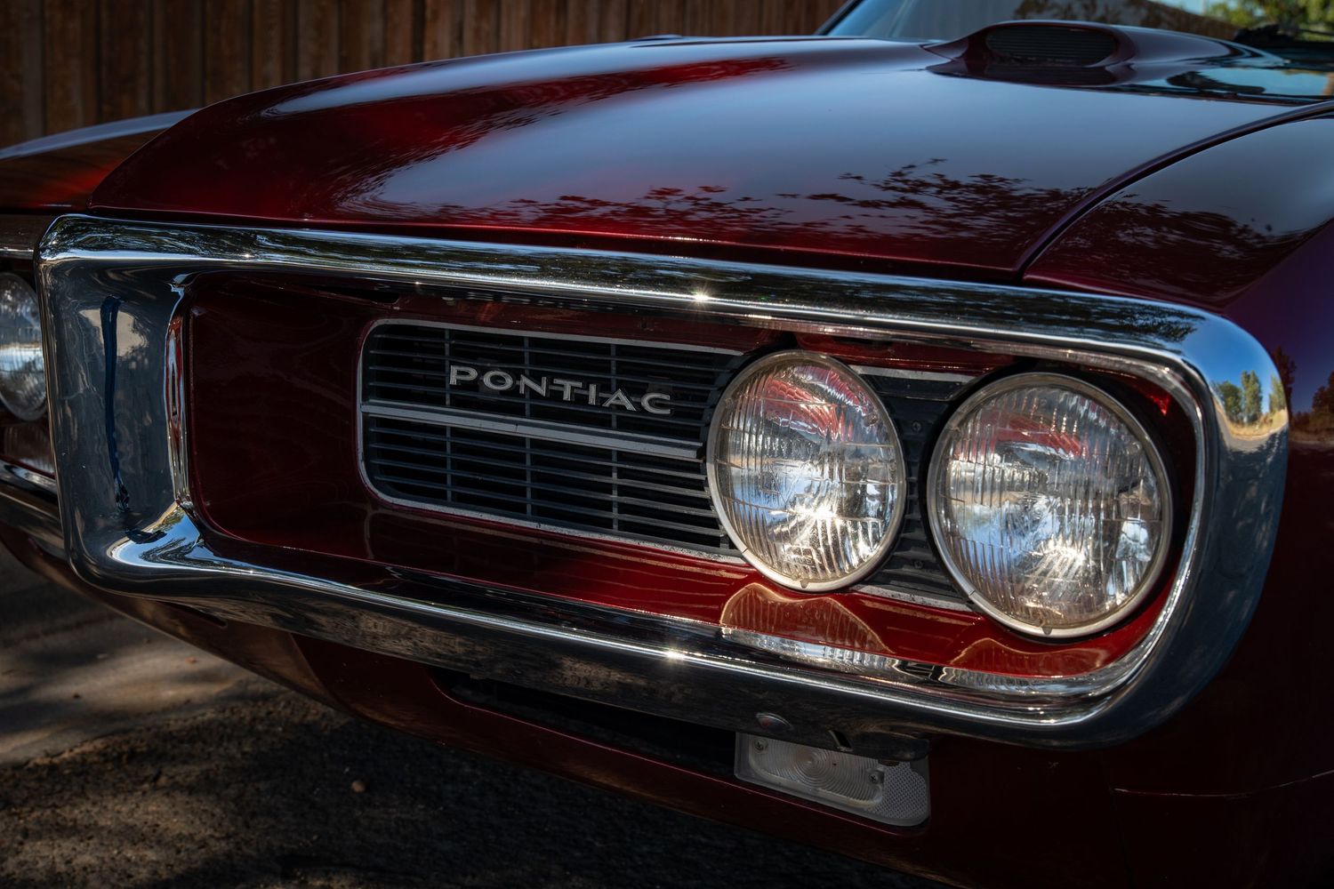Close-up of a classic Pontiac muscle car front grille with chrome details and dual headlights in deep red.
