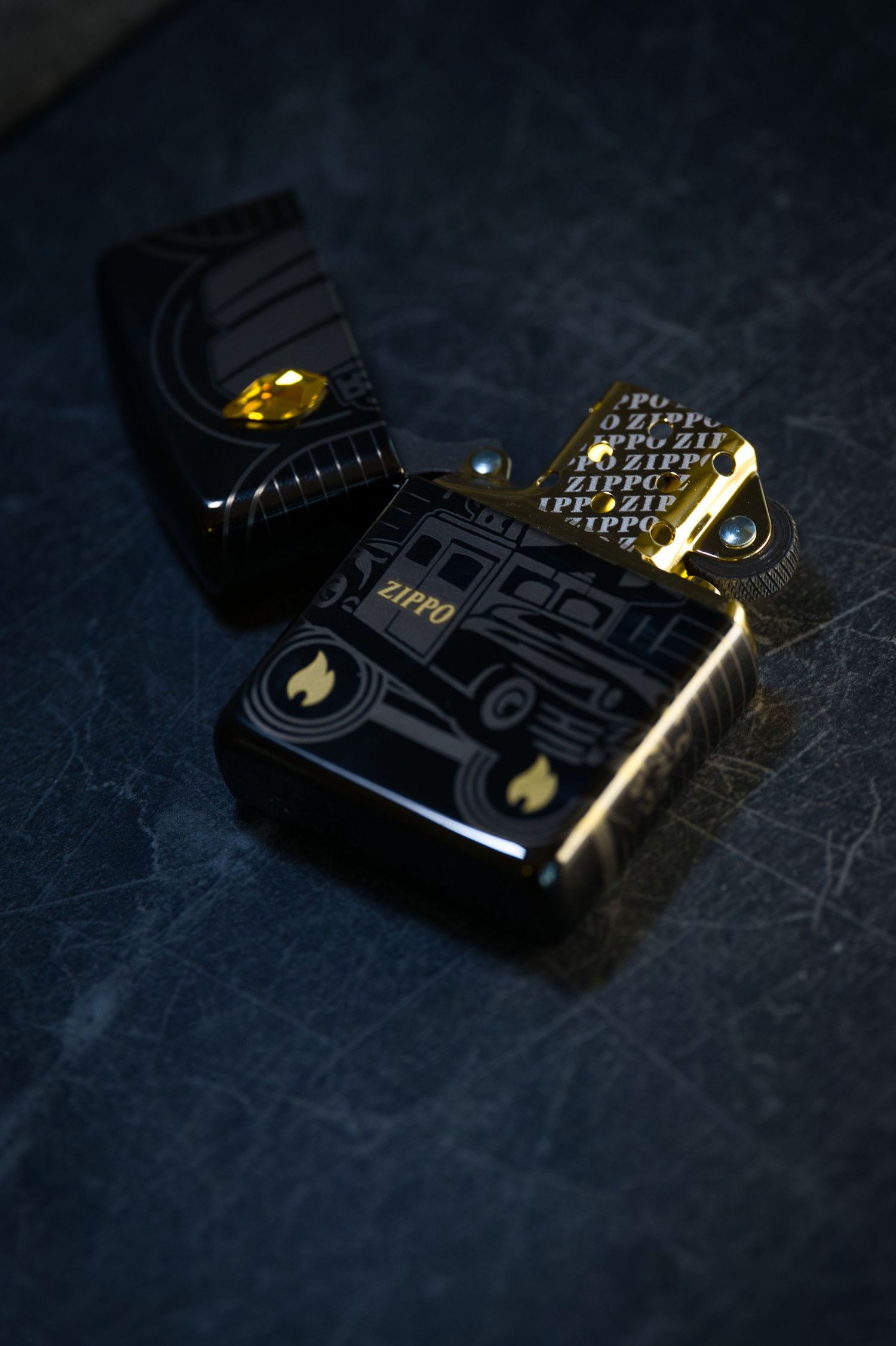 Black and gold Zippo lighter open on dark textured surface with decorative engravings.