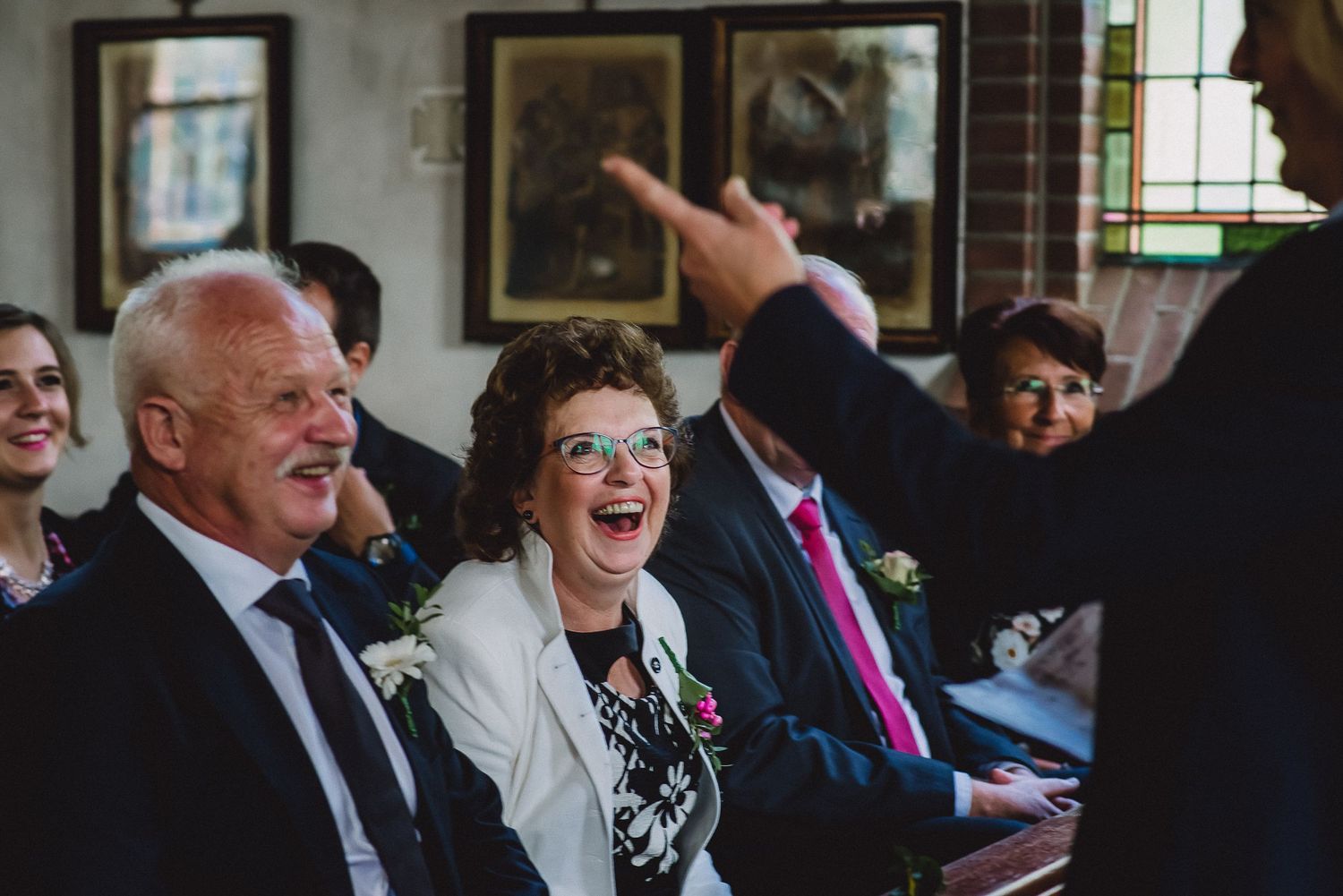 Joyful wedding guests laughing during a church ceremony, with an elderly woman smiling broadly.