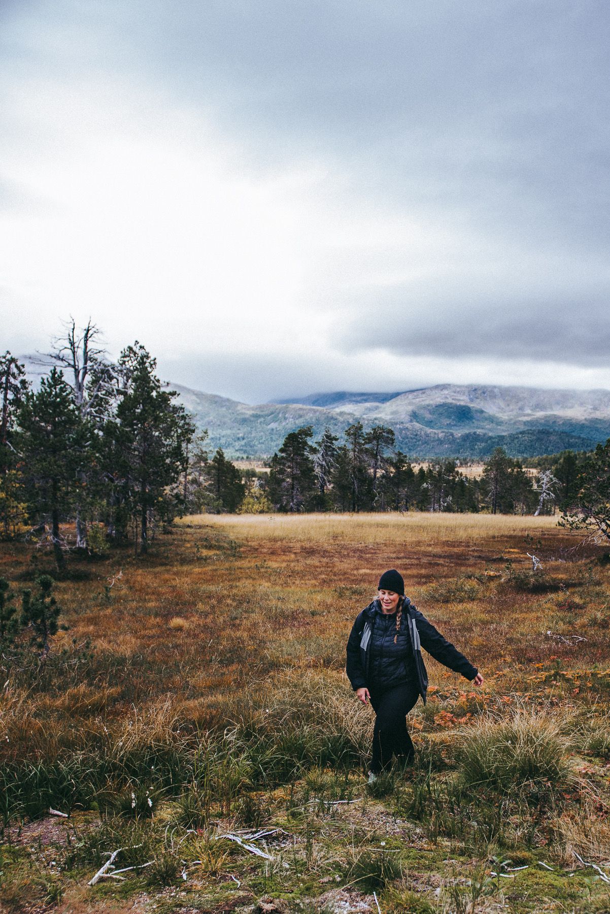 Solo hiker walking through vast open autumn moorland with misty mountains in the background.