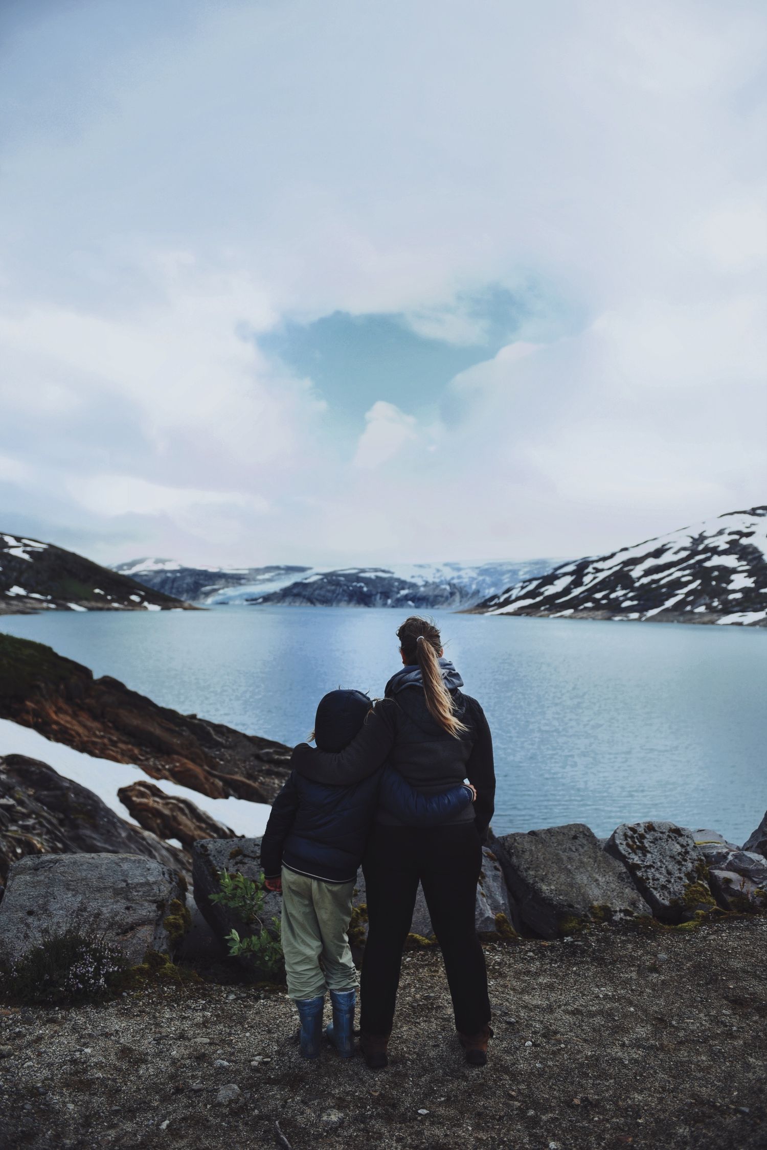Mother and child gazing at a stunning snow-capped mountain lake landscape in Norway.