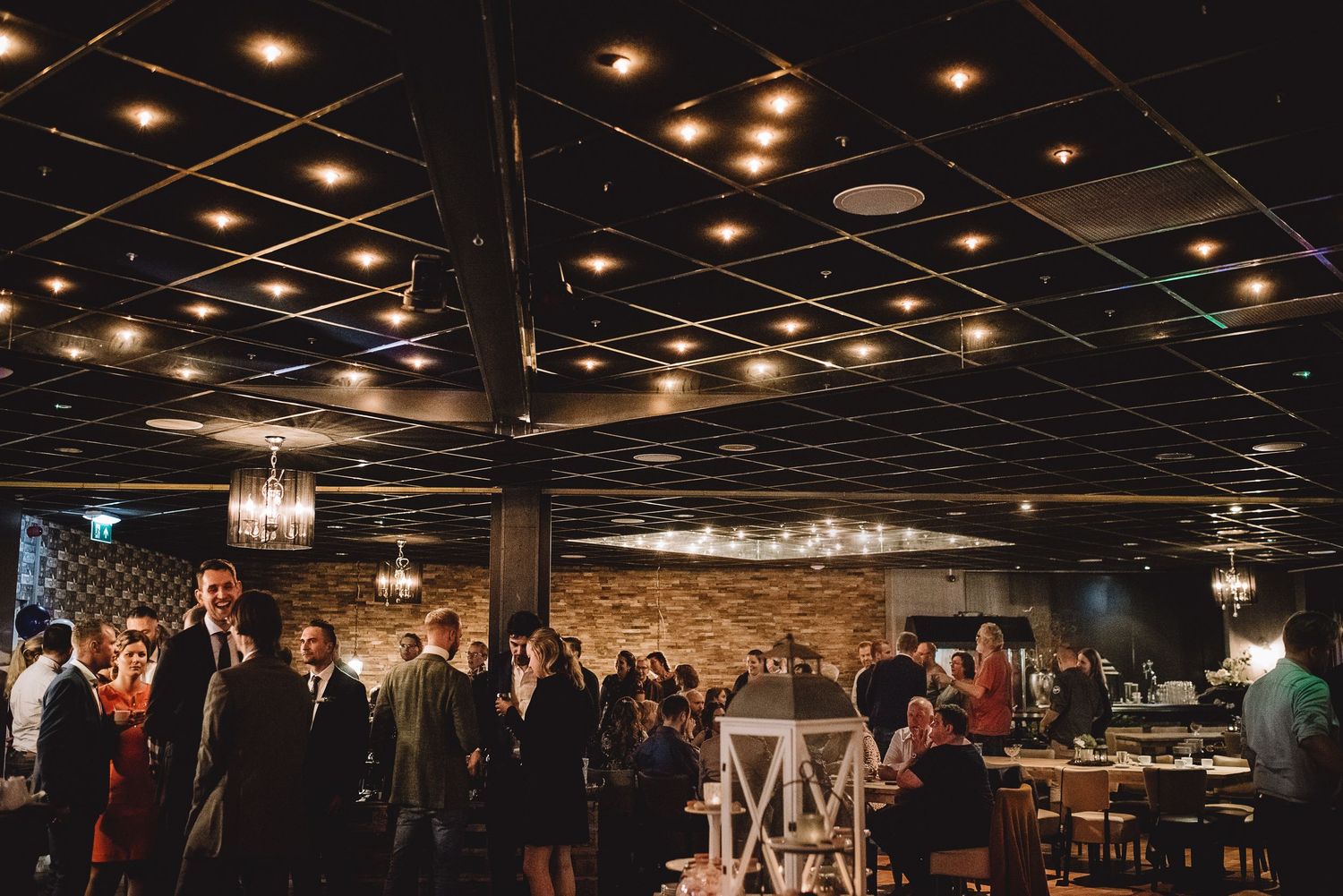 Elegant wedding reception venue with guests mingling under a dark ceiling with warm lights.