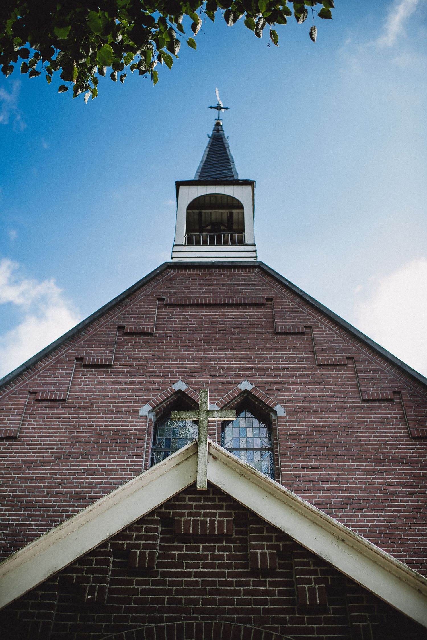 Low-angle view of a red brick church steeple with a cross against a bright blue sky.Door Kim van de Broek Fotografie