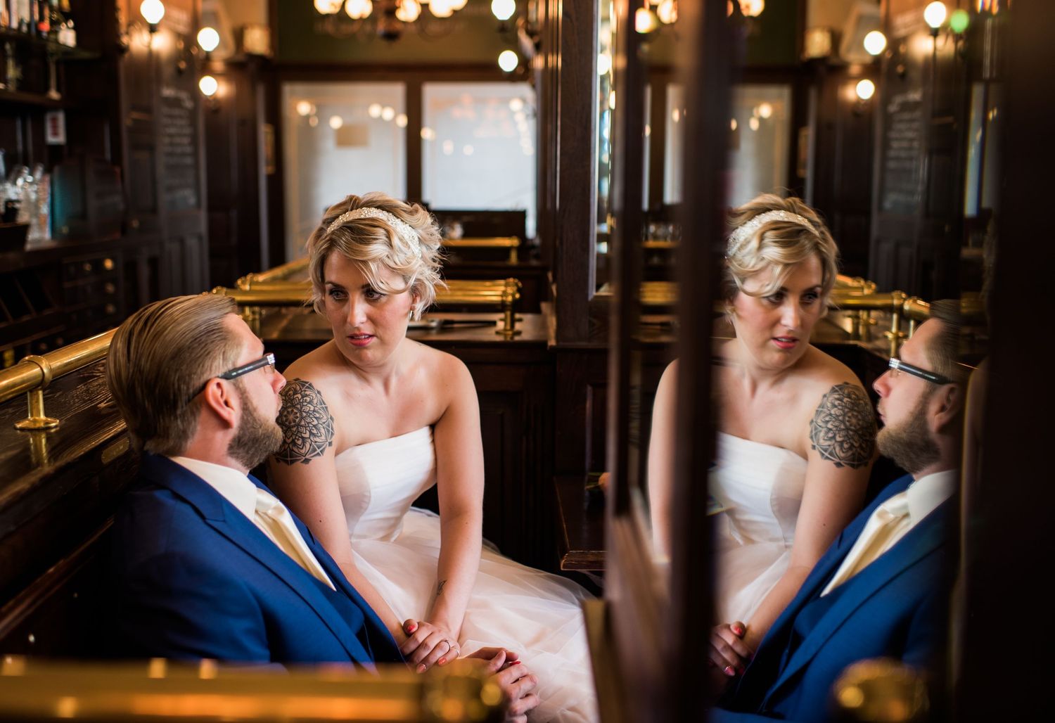 Bride and groom in blue suit reflected in bar mirror, sharing an intimate moment at wedding venue. Door Kim van de Broek Fotografie