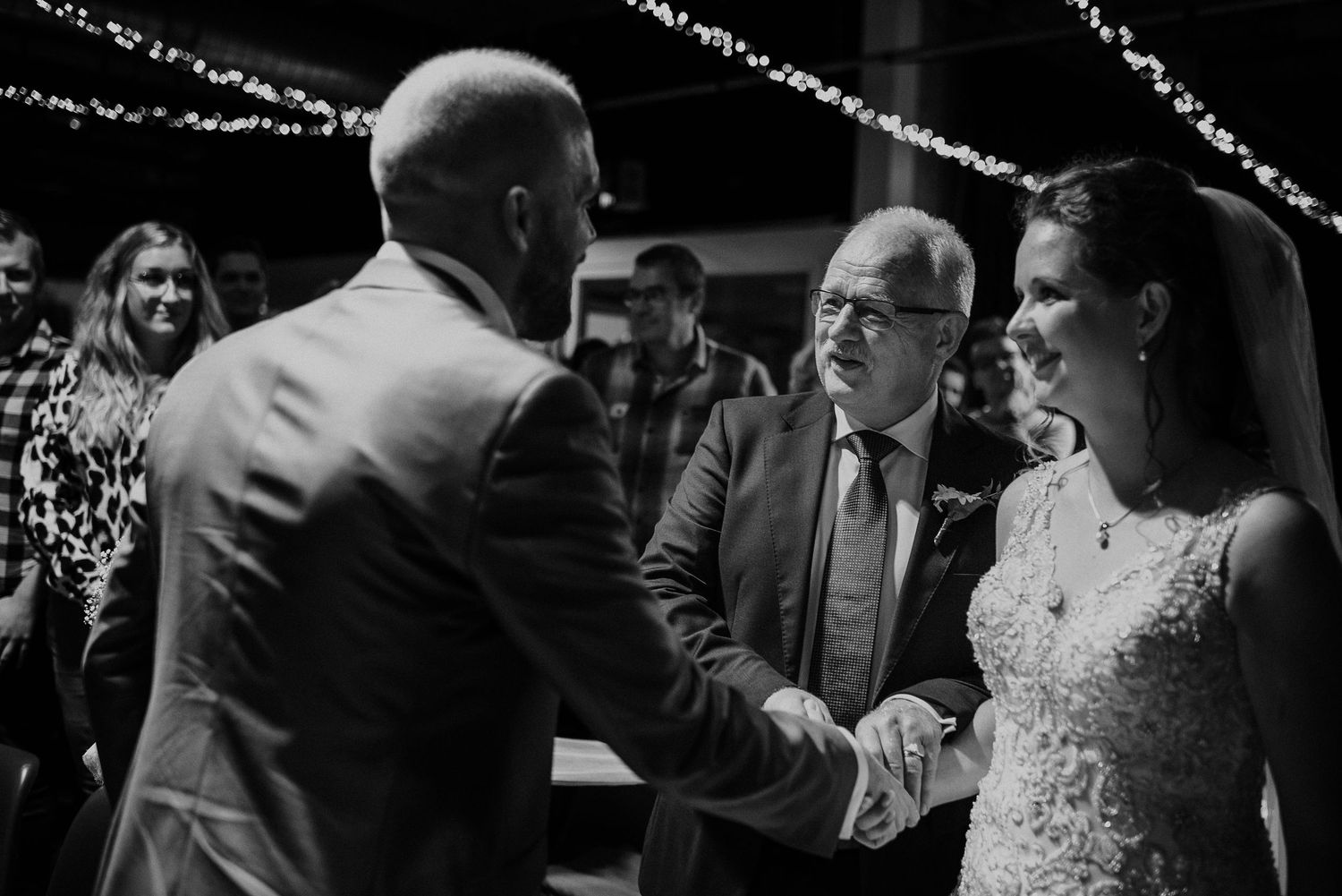 Black and white photo of wedding guests greeting the bride and groom with a warm handshake. Door Kim van de Broek Fotografie