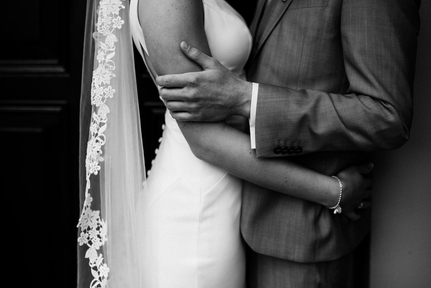 Black and white close-up of bride and groom embracing, showing wedding dress and lace veil.