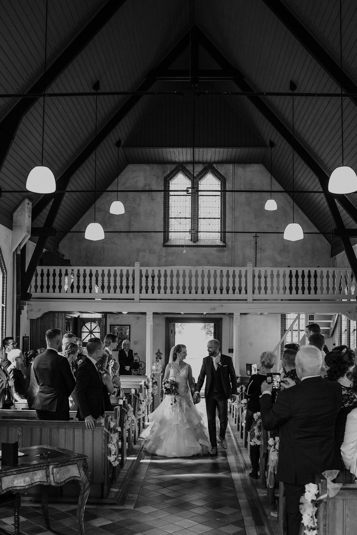 Bride walks down the aisle with escort in a charming wooden church filled with wedding guests.