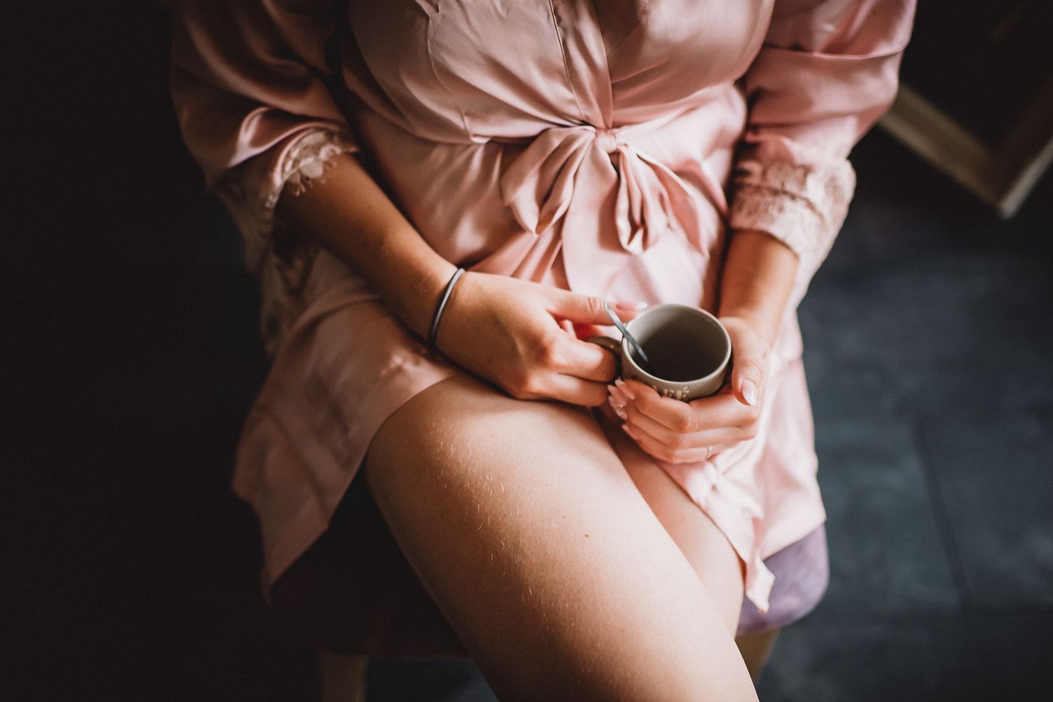 Bride in pink robe holds a coffee cup during wedding morning preparations.