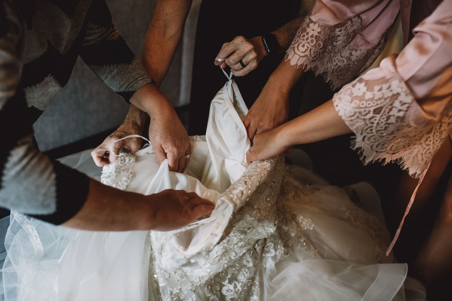 Bridesmaids help bride into her intricate lace wedding gown during bridal preparations.