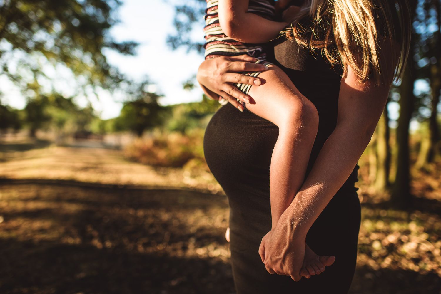 Close-up of pregnant woman cradling baby bump outdoors in sunny park.
