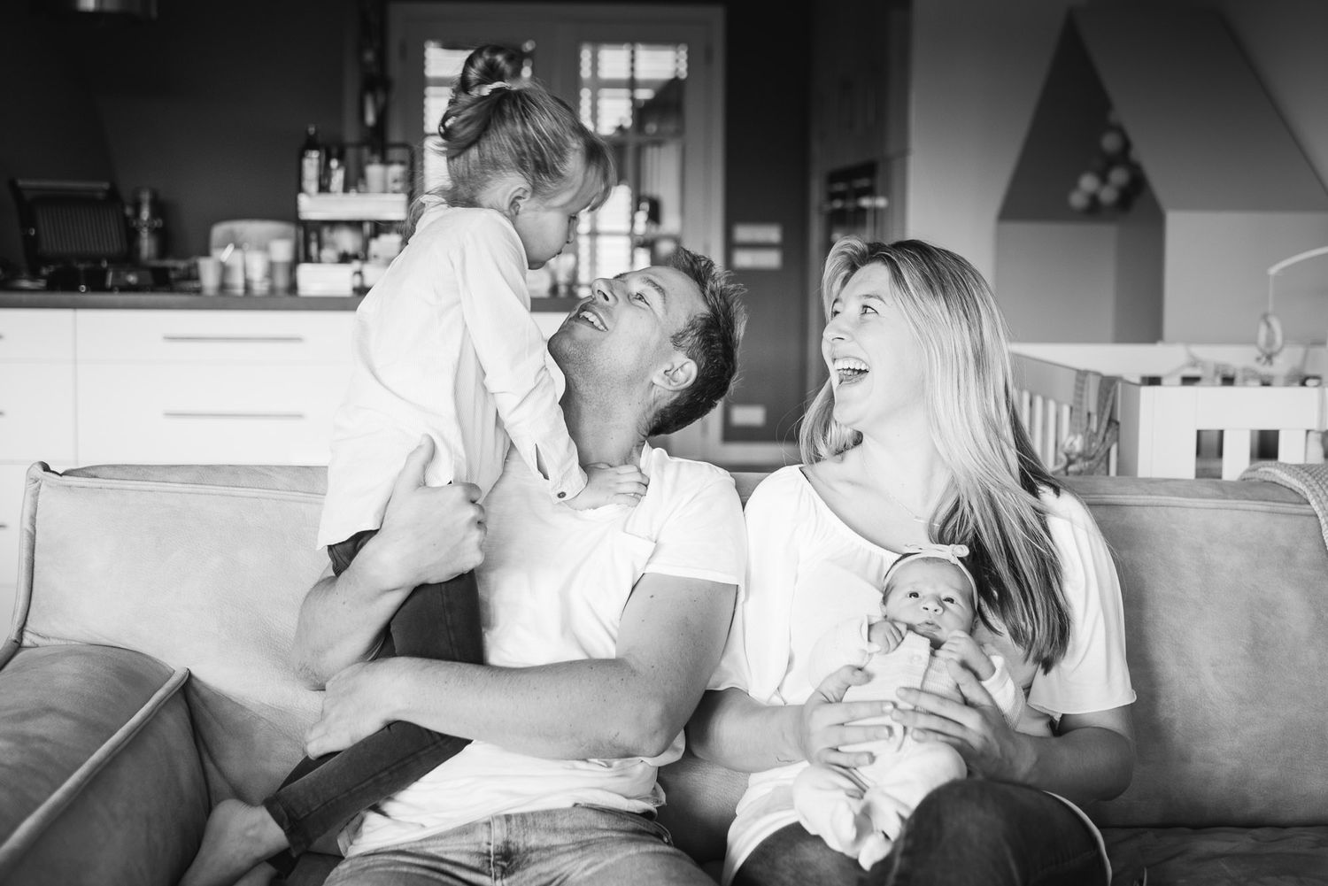 Happy family laughing together on sofa with toddler and newborn baby.