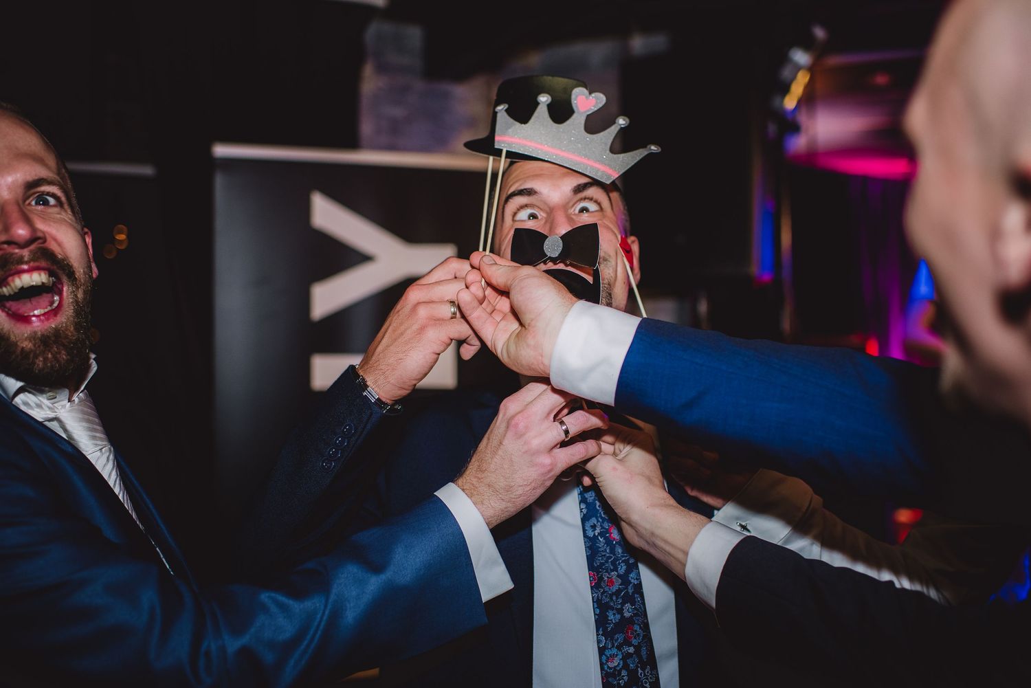 Wedding guests laughing while holding photo booth props including a crown and mustache.