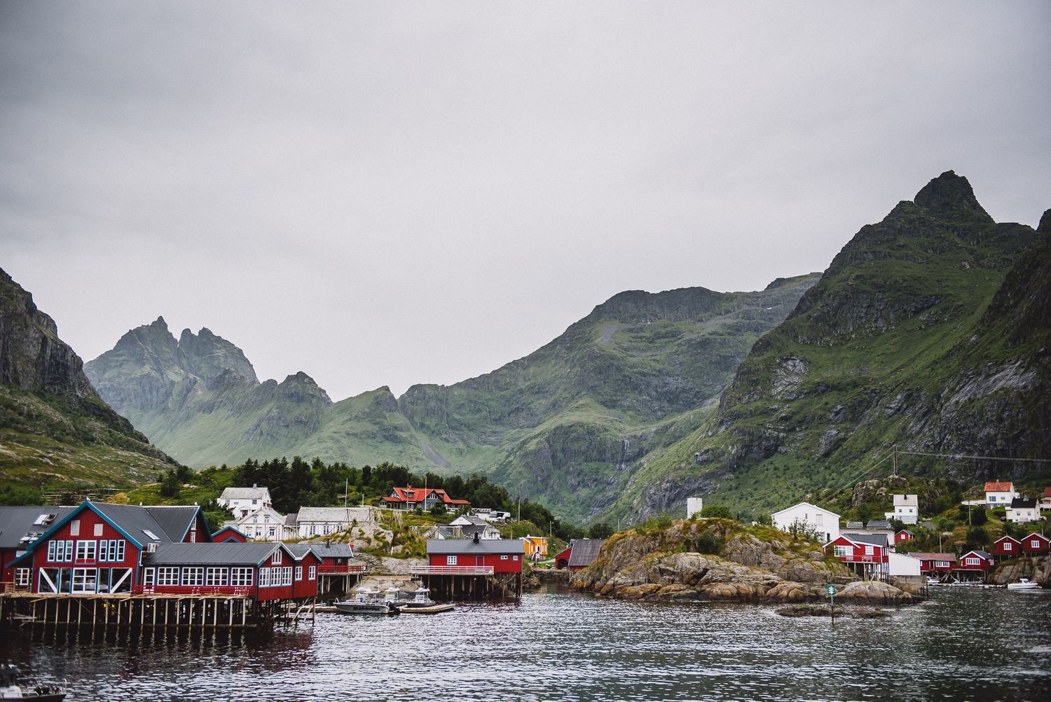 Colorful red and white fishing village nestled beneath dramatic green mountains in Lofoten, Norway.