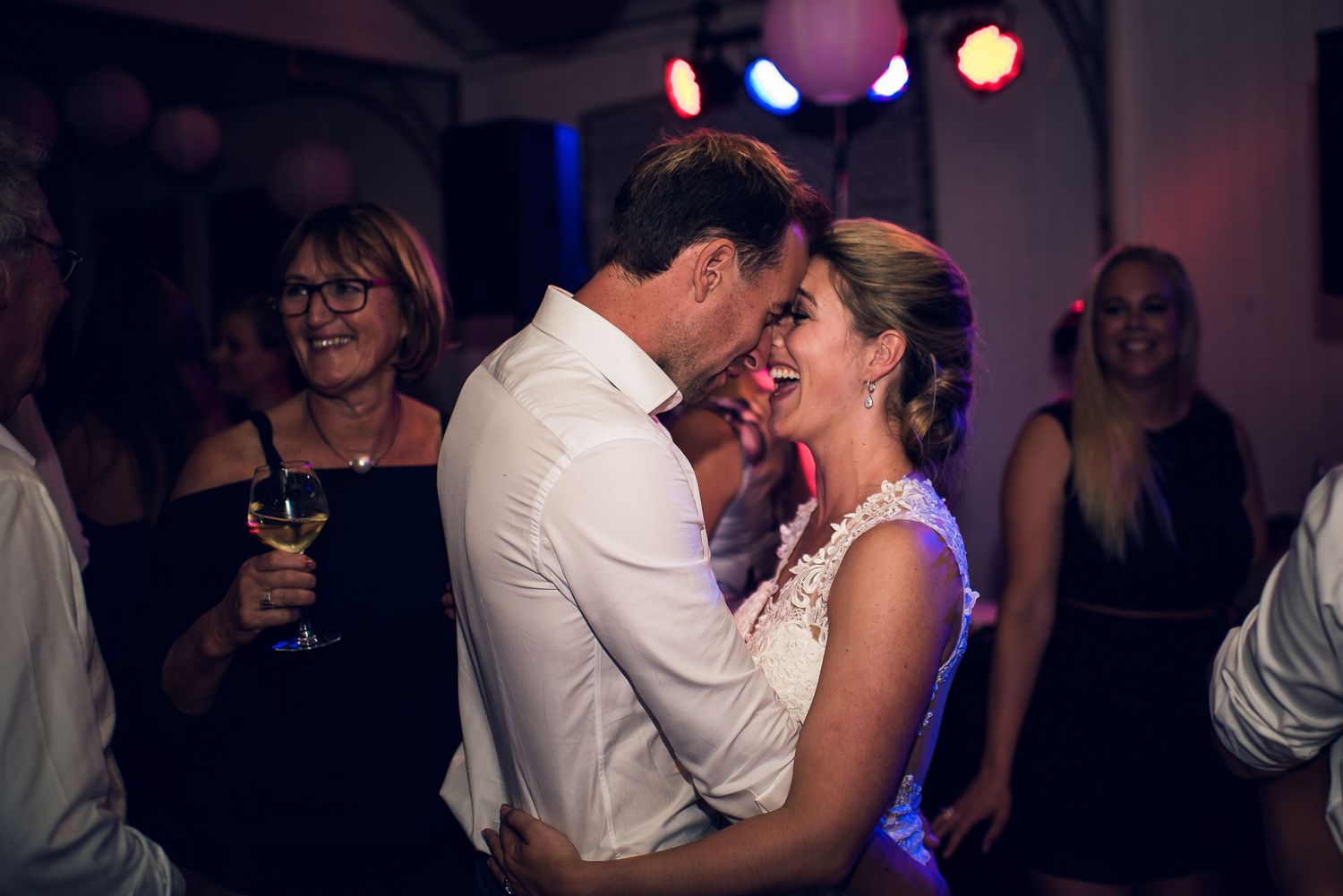 Bride and groom sharing romantic dance under colorful lights at lively wedding reception party. wedding photography