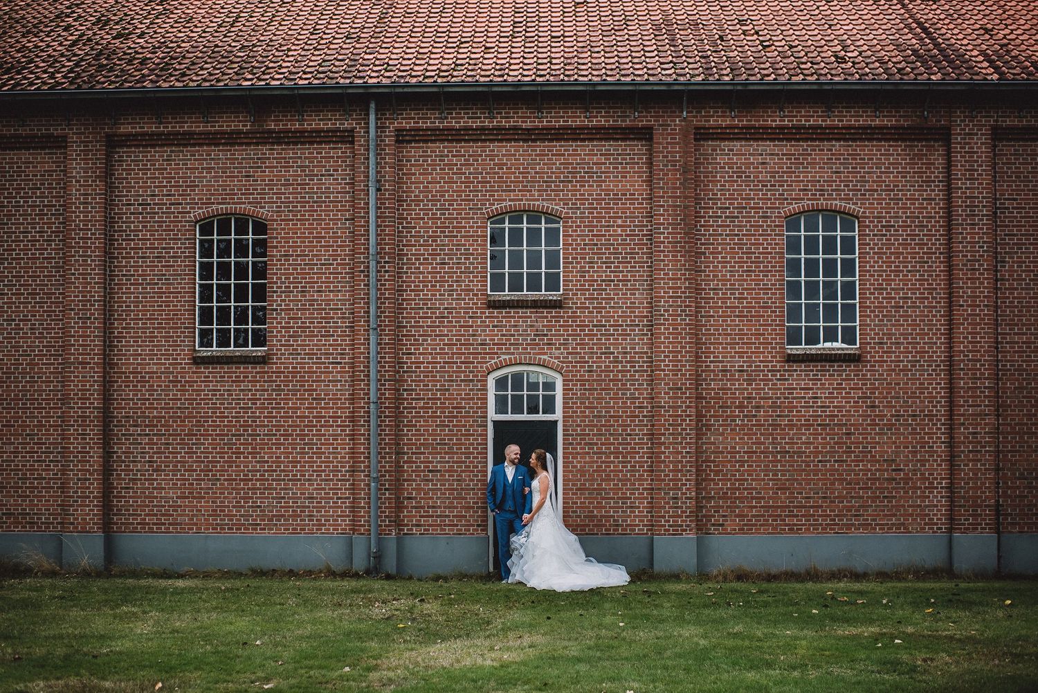 Wedding couple posing in front of a large red brick building with arched windows on their special day.