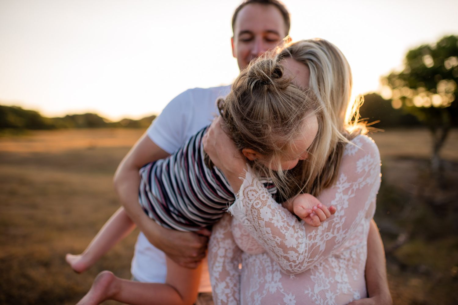 Family at golden sunset with father holding child who leans into mother in a dry field.
