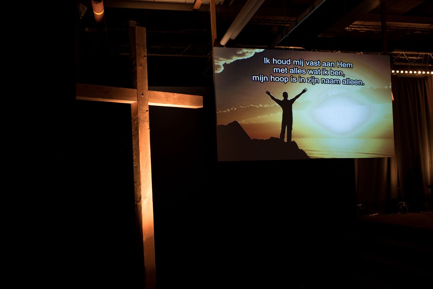 Wooden cross beside a projection screen displaying worship lyrics at a wedding ceremony venue.