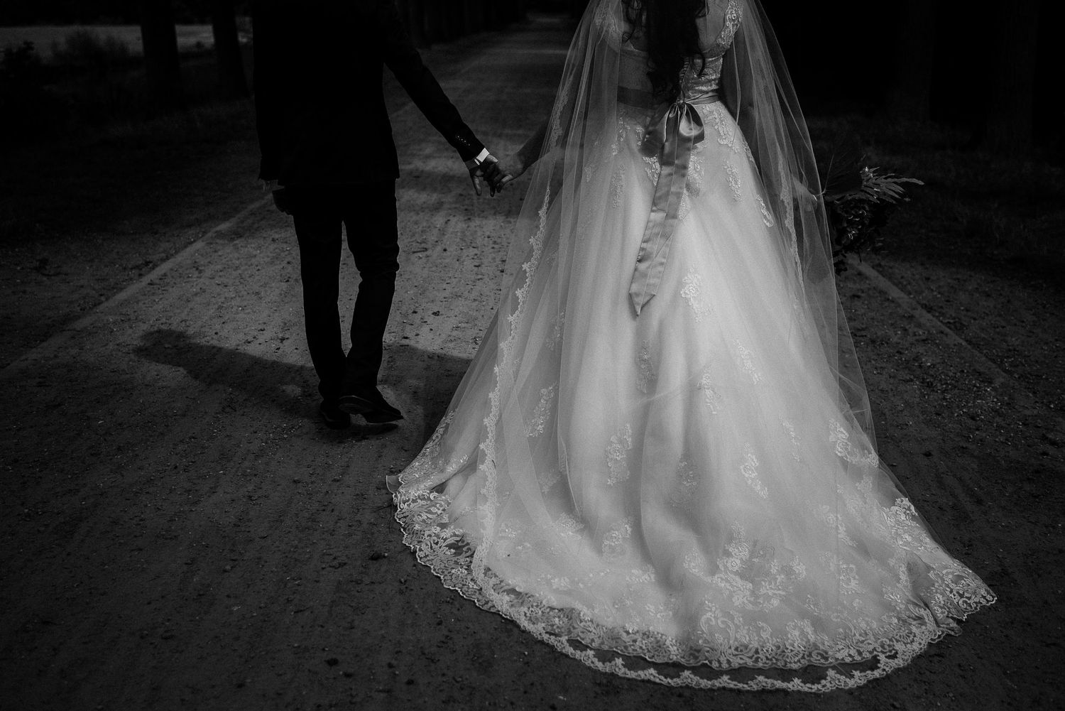 A bride and groom walk hand in hand, showcasing the intricate lace train of her elegant wedding gown.wedding photography