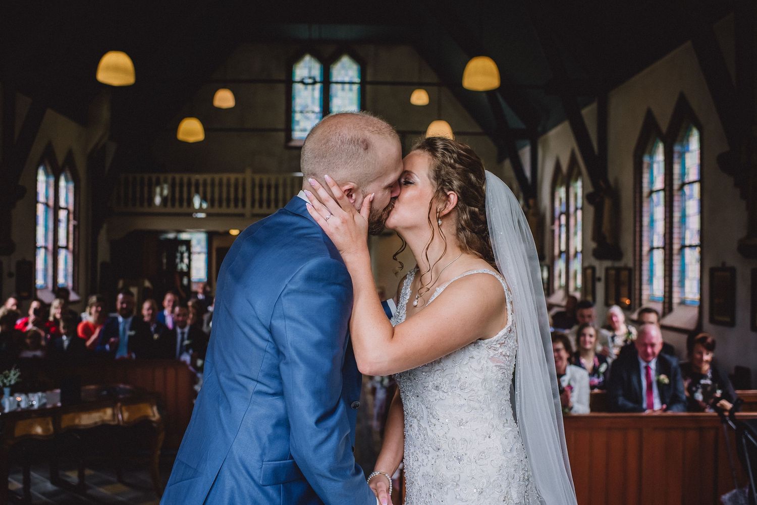Bride and groom share their first kiss at the altar surrounded by wedding guests in a church.