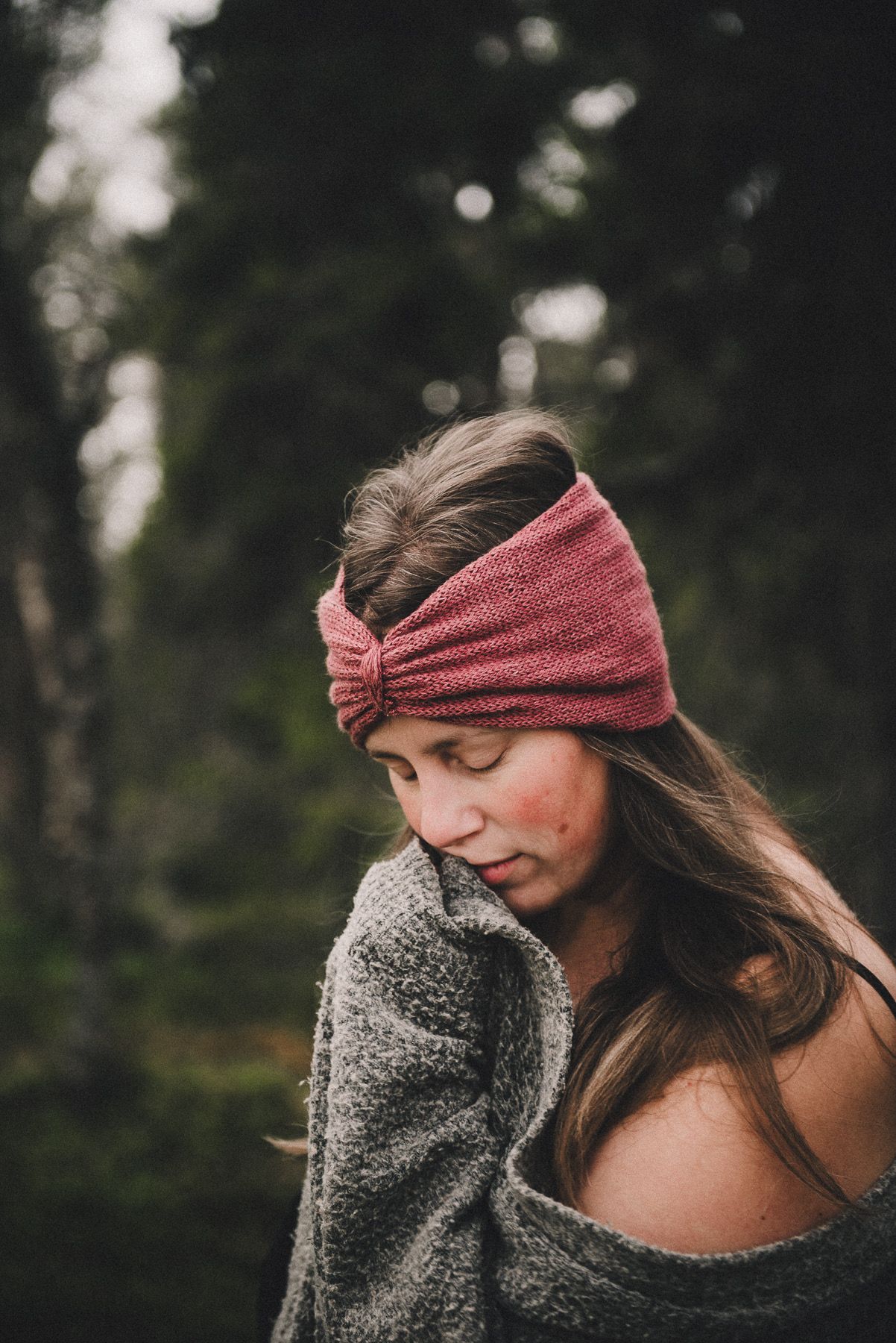 Young woman wearing a pink knit headband in a moody forest setting.