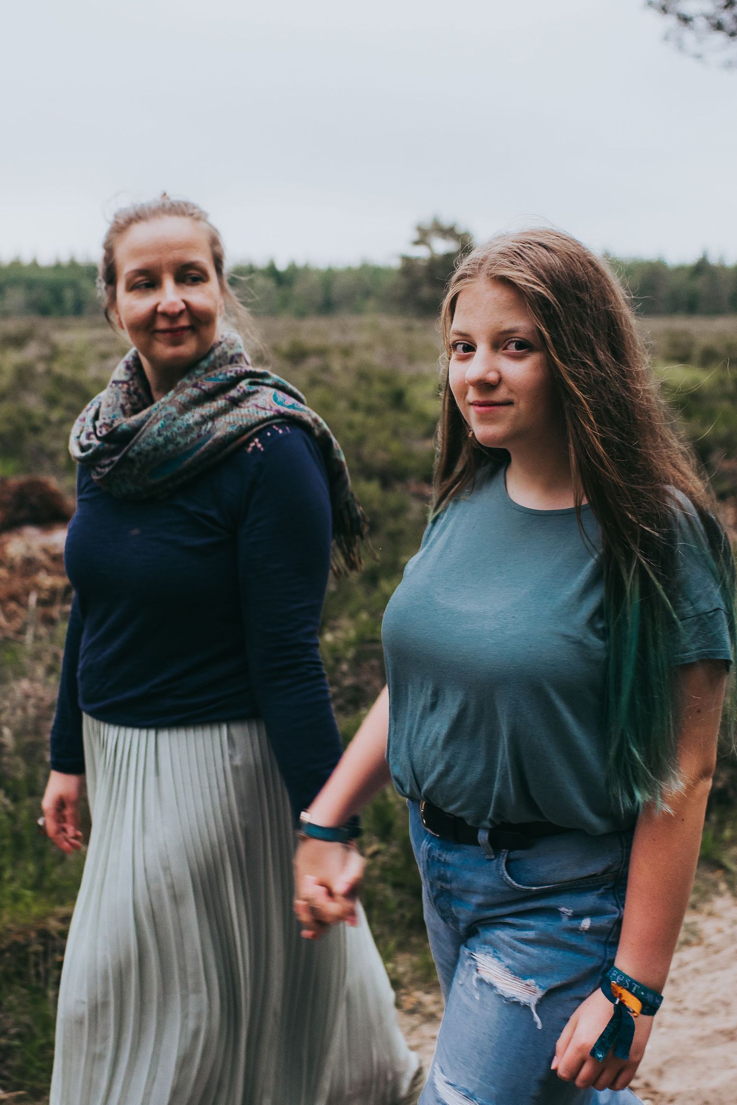 Mother and teenage daughter holding hands while walking on a scenic nature path.