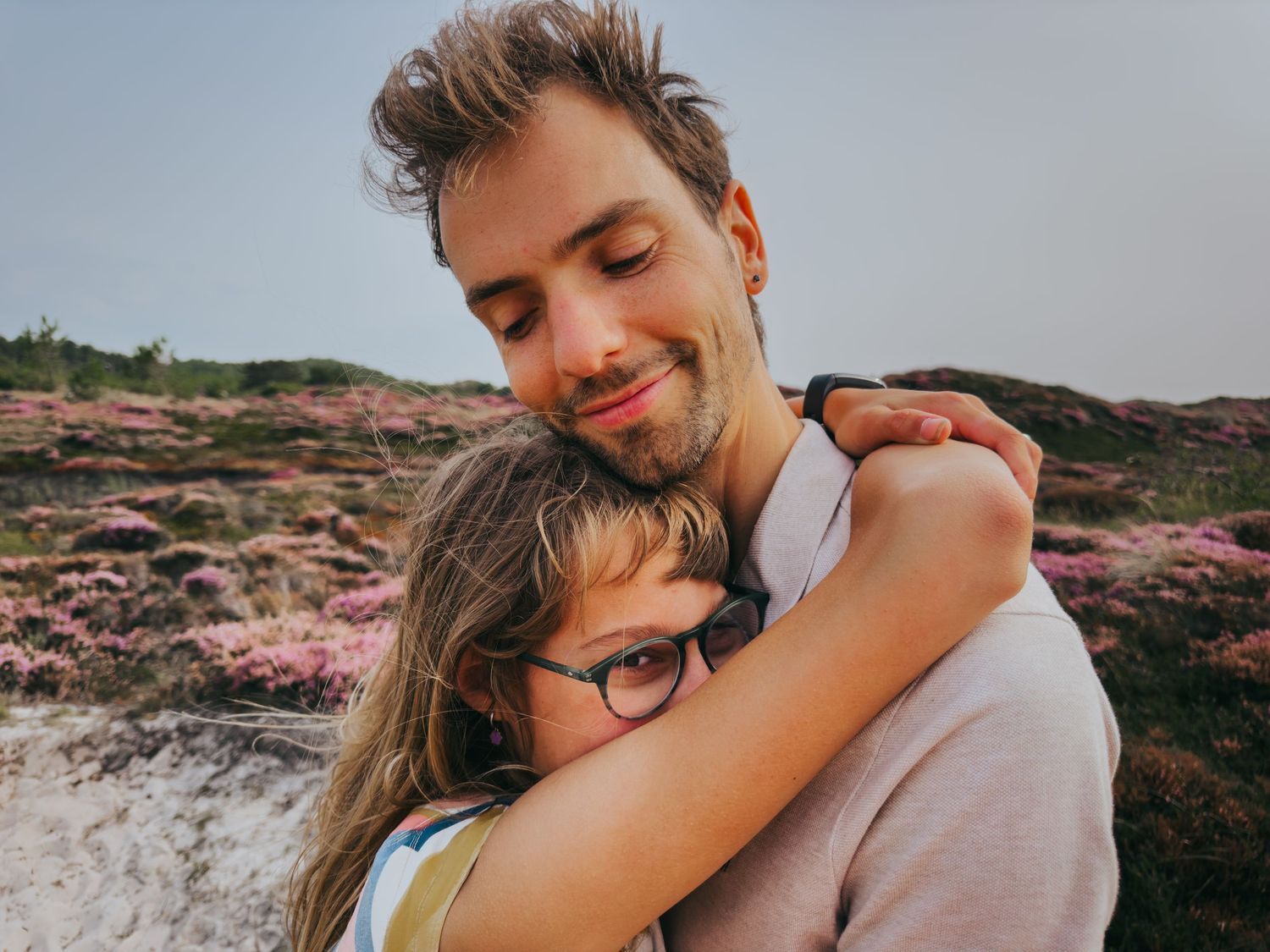 Father and child sharing a warm embrace outdoors with purple heather fields.