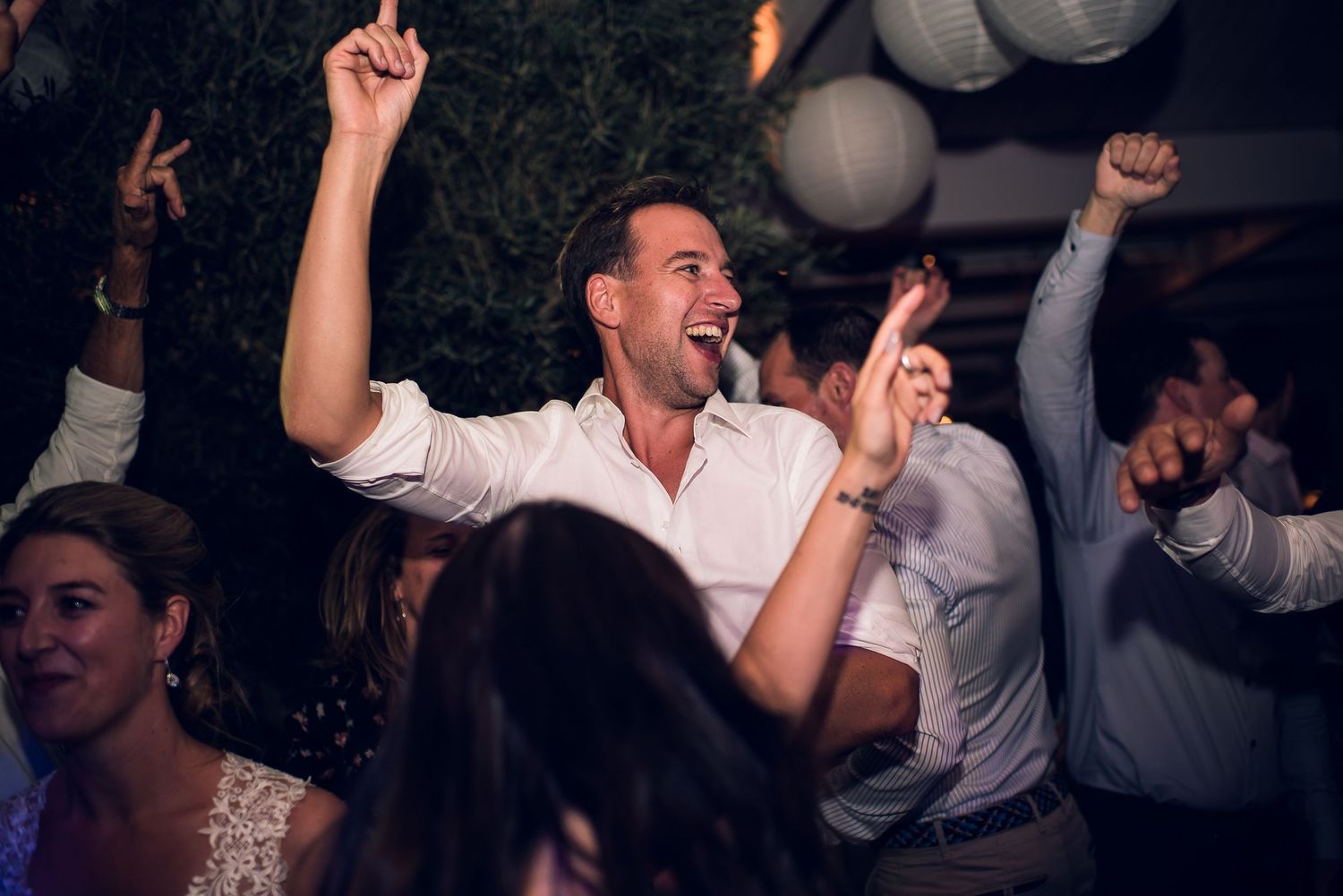 Joyful wedding guest dancing with arms raised and laughing at an outdoor evening reception party.