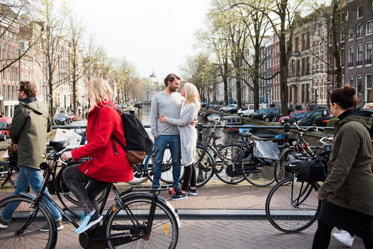 Romantic couple sharing a kiss on an Amsterdam canal bridge surrounded by bicycles.