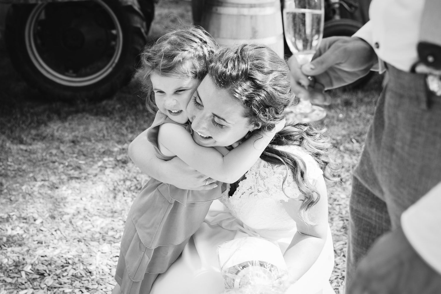 Black and white photo of bride joyfully hugging a young flower girl at an outdoor wedding reception.