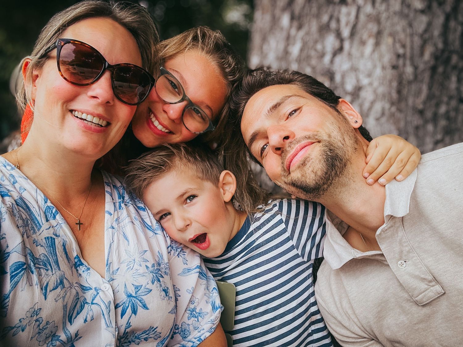 Joyful family of four taking a fun selfie together near a tree.