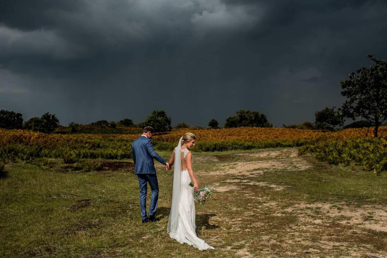 Bride and groom stand in a vineyard field under dramatic stormy dark skies on their wedding day.