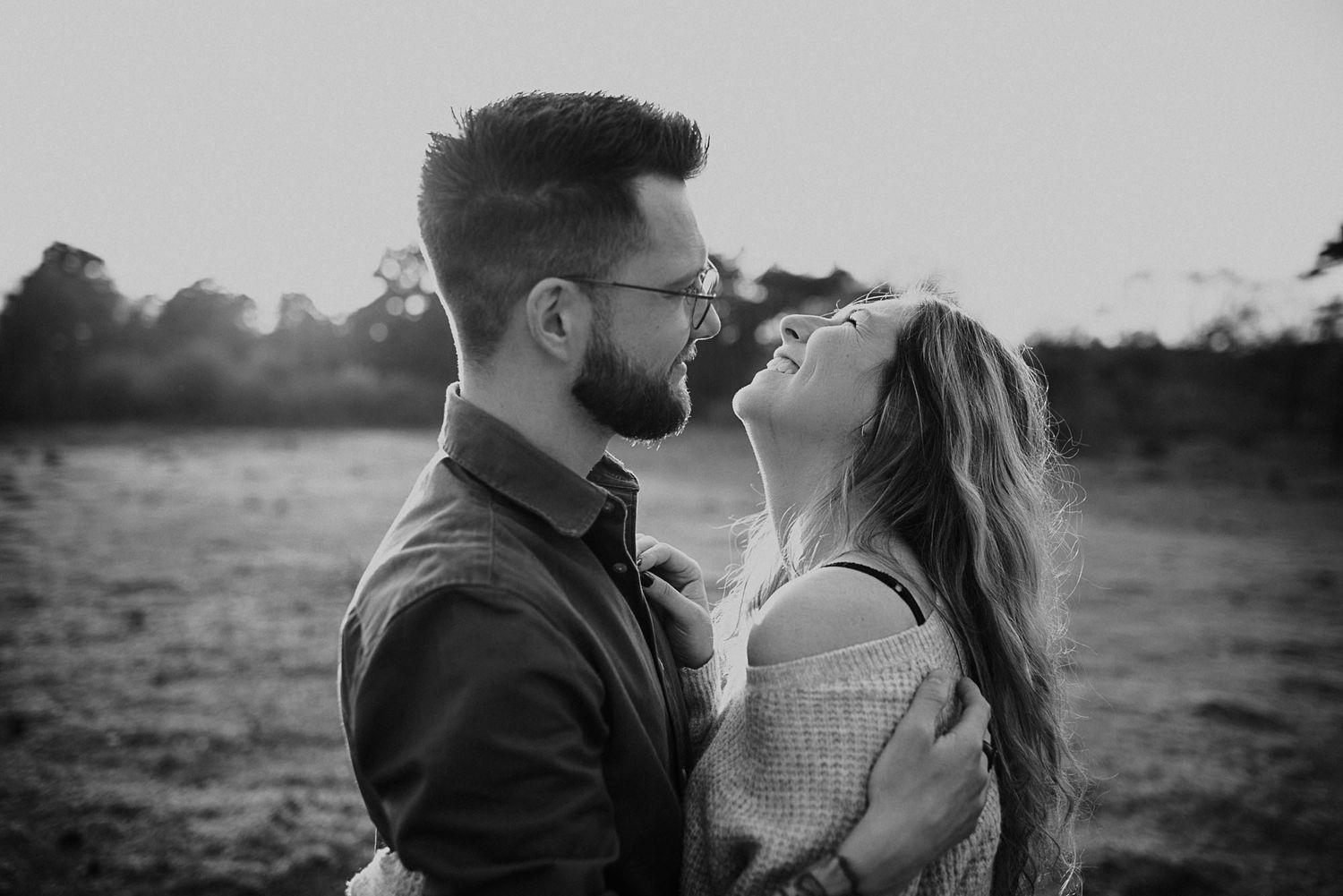 Romantic black and white photo of couple gazing at each other in golden field at sunset.