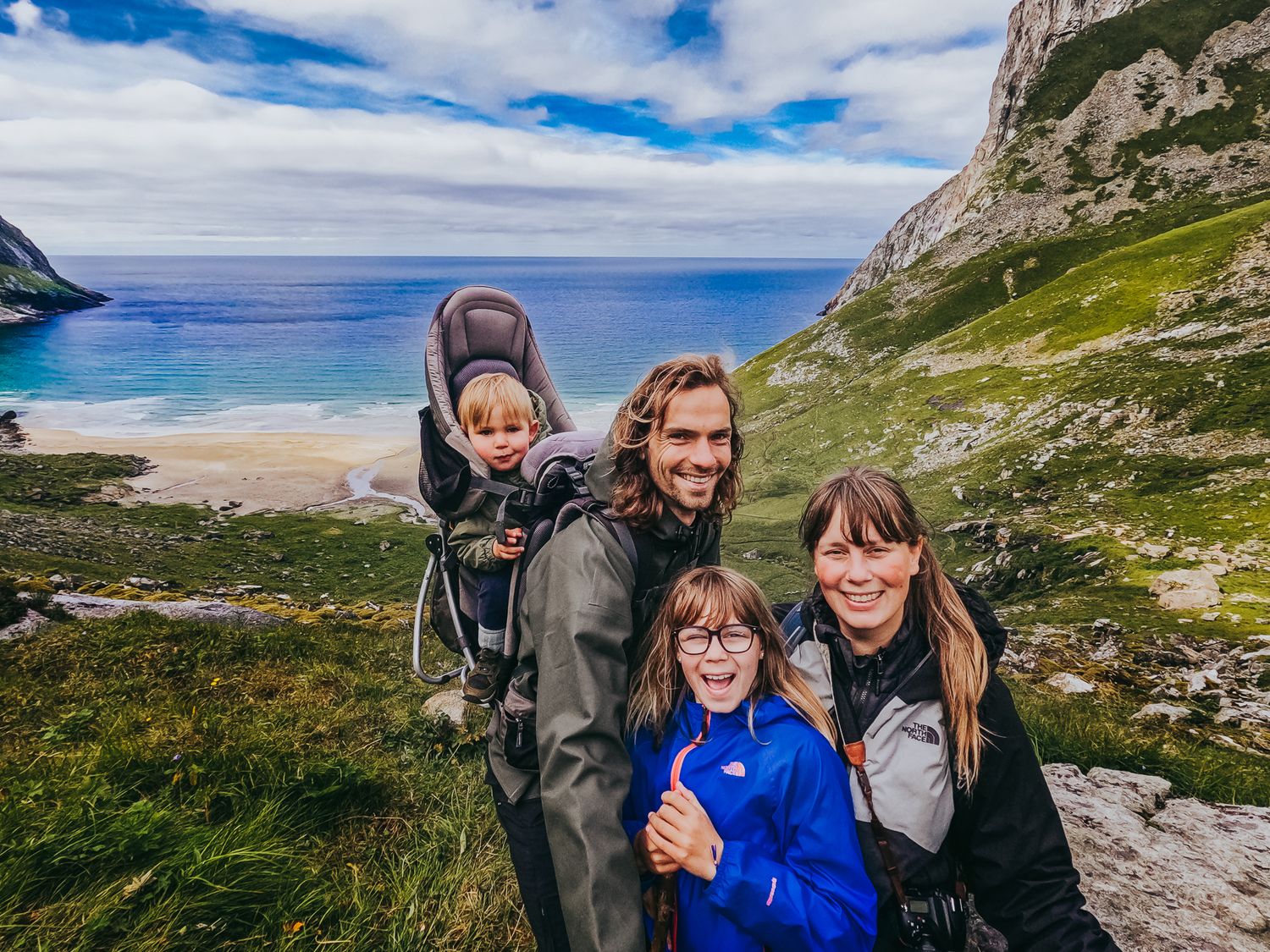 Happy family of four posing with scenic Norwegian coastal cliffs and turquoise sea behind them.