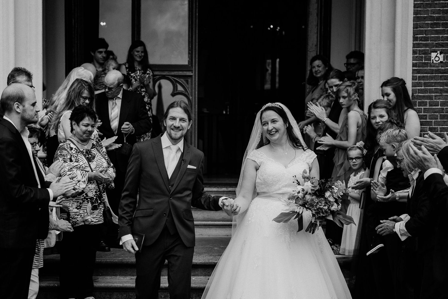 A smiling bride and groom exit a classic building as guests applaud and celebrate their wedding ceremony. wedding photography