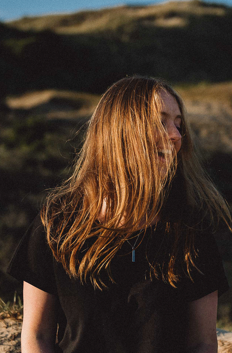 Young woman with long golden hair blowing over her face outdoors in natural sunlight.Door Kim van de Broek Fotografie