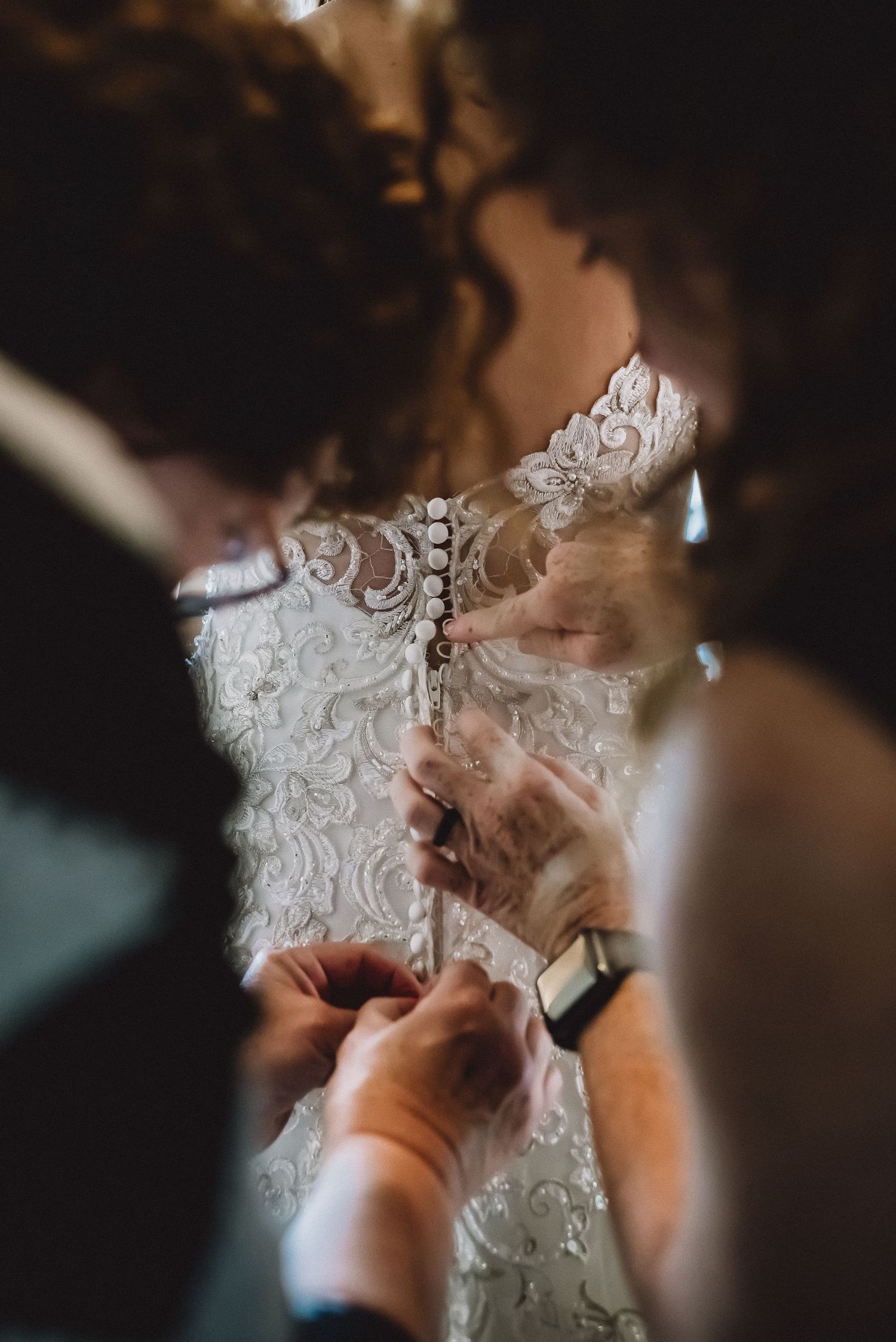 Close-up of hands carefully buttoning the intricate lace back of a bride's elegant wedding dress. gefotografeerd door Kim van den Broek