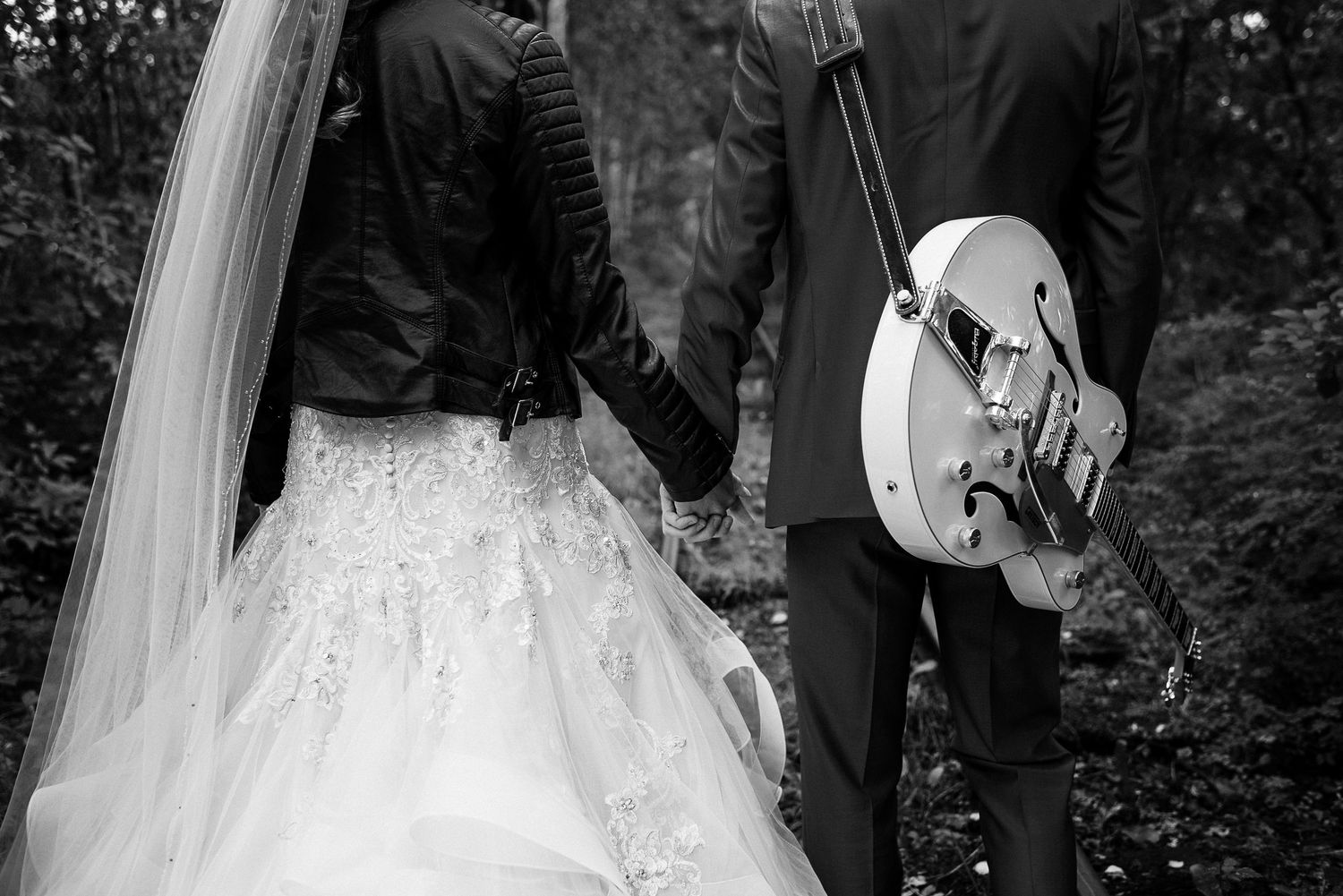 Black and white photo of bride and groom walking hand in hand with a vintage guitar.
