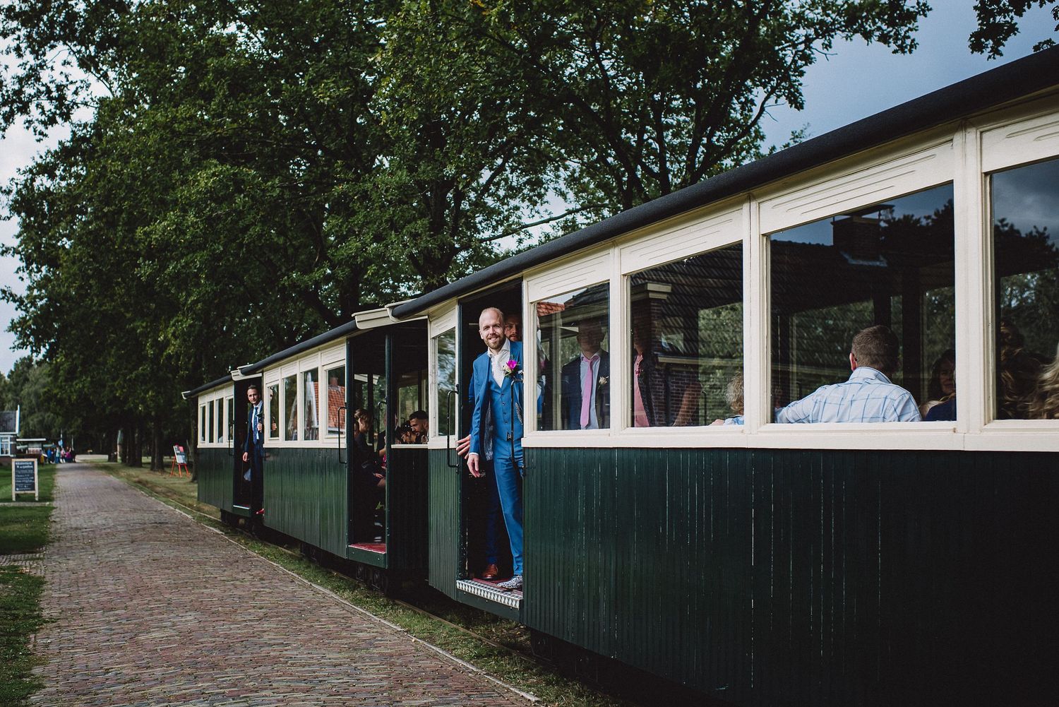Groom in blue suit standing at the door of a vintage green and cream passenger train car.