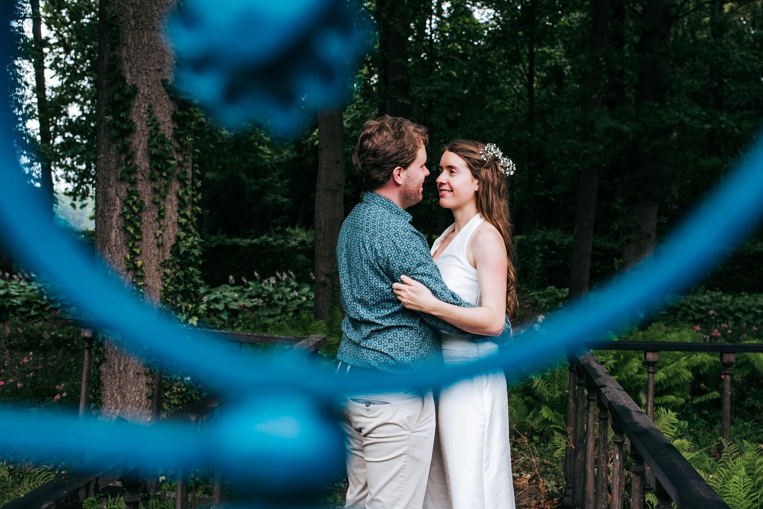 Couple sharing a romantic moment framed by blue ironwork in a lush forest.