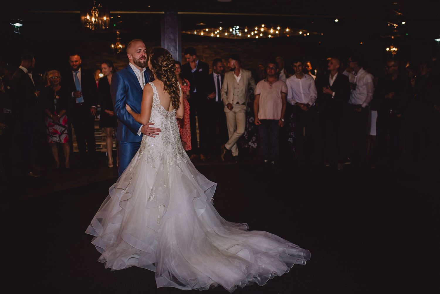 Bride in a stunning white gown and groom on the dance floor surrounded by wedding guests, door Kim van den Broek