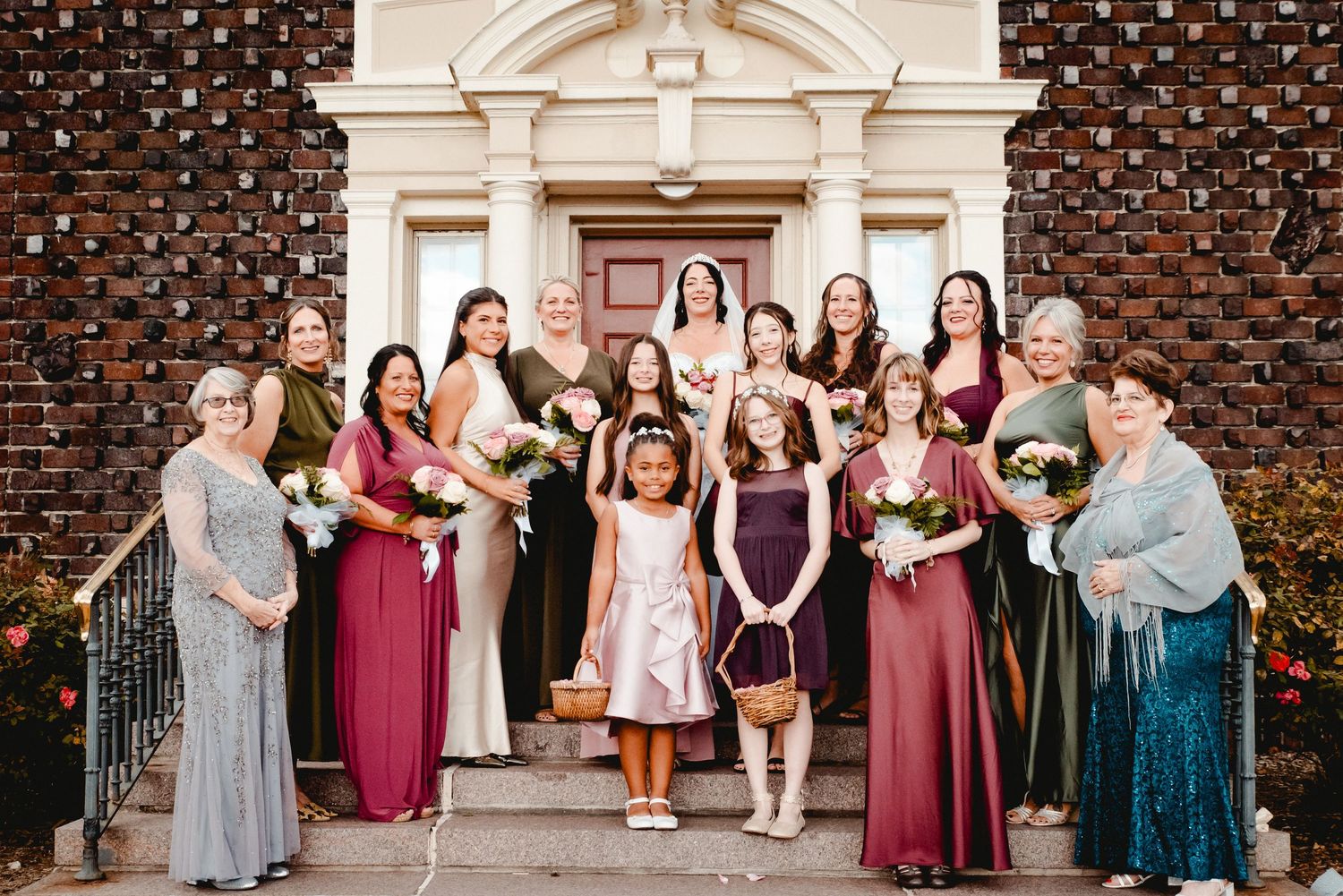 The bride poses with her bridesmaids, mother, mother of the groom, and the flower girls after a fun day getting ready in Johnson City, NY.