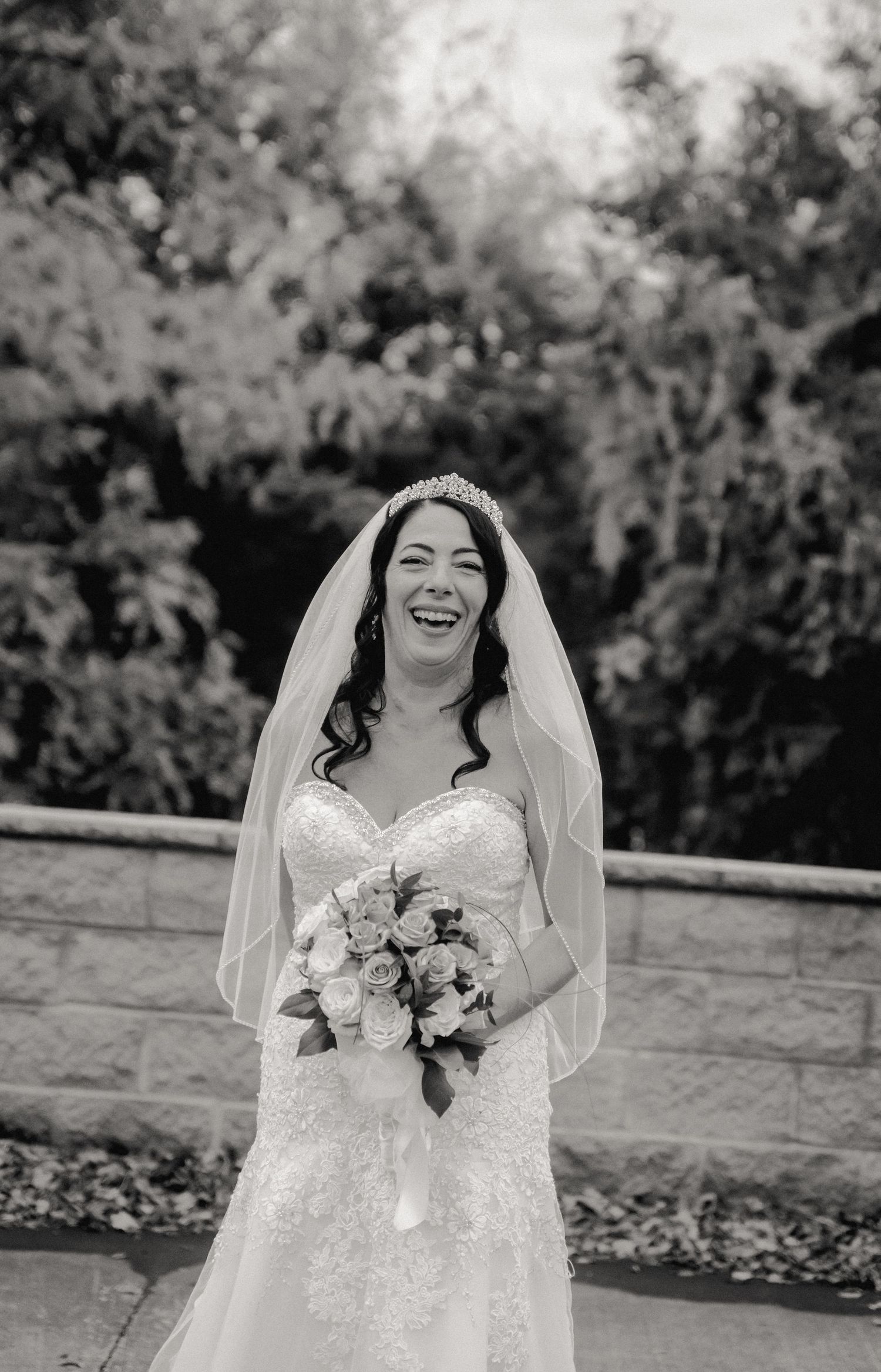 A timeless black and white portrait of a bride laughing. She is holding her bouquet and has her veil held up by a sparkling tiara.